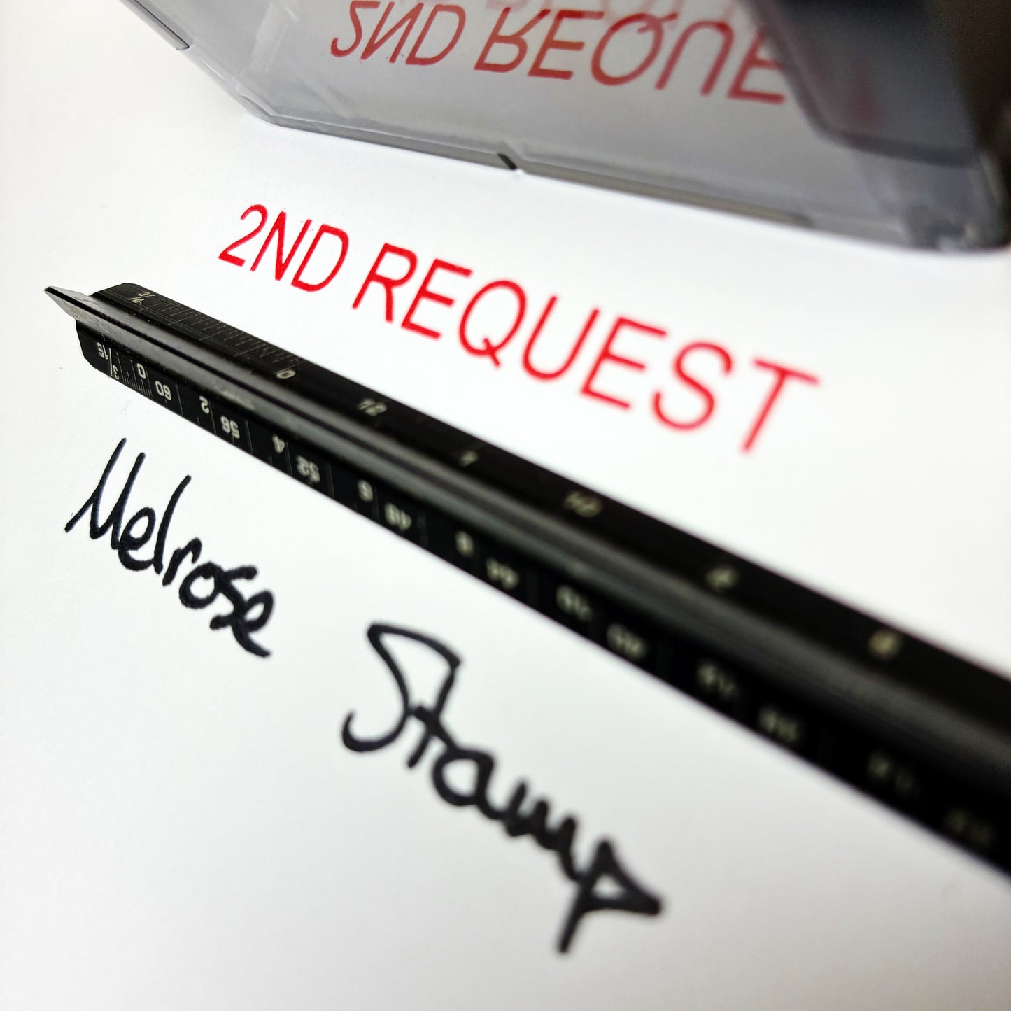 Close-up of a document with '2nd Request' and 'Melrose Stamp' written on it, with a stamp in the background.