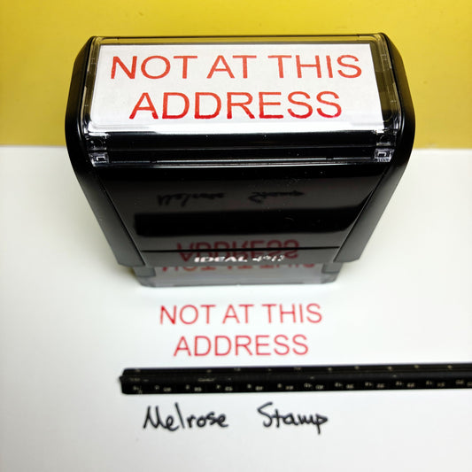 Rubber stamp with 'Not at this address' text on a white surface with a yellow background