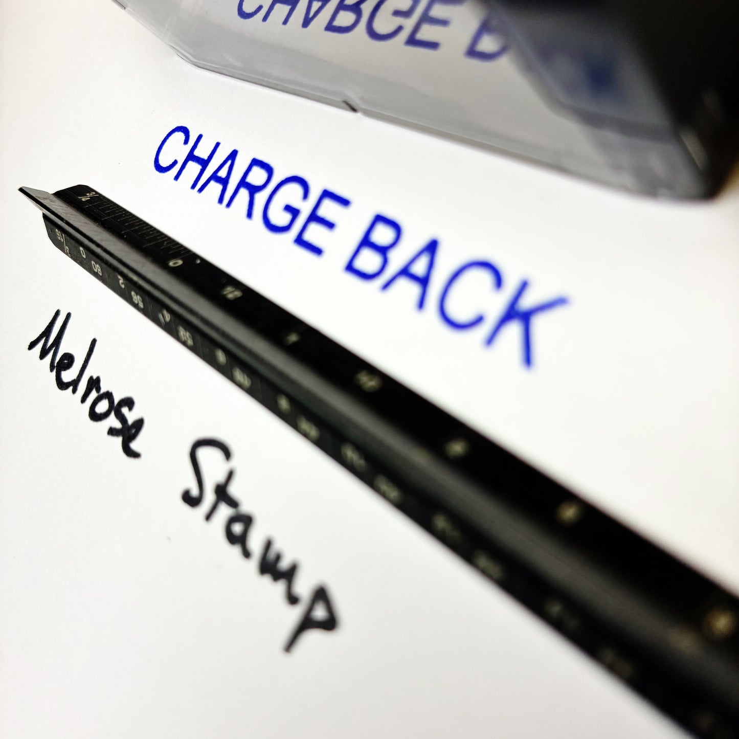 Close-up of a stamp with 'Melrose Stamp' and 'Charge Back' text on a white background.