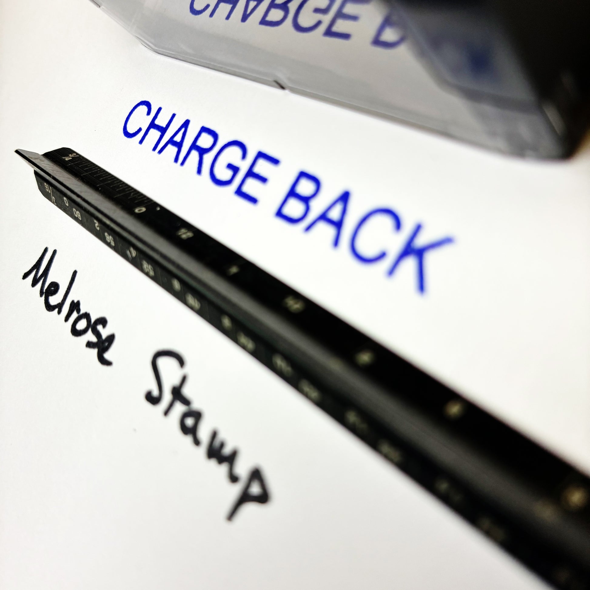 Close-up of a stamp with 'Melrose Stamp' and 'Charge Back' text on a white background.