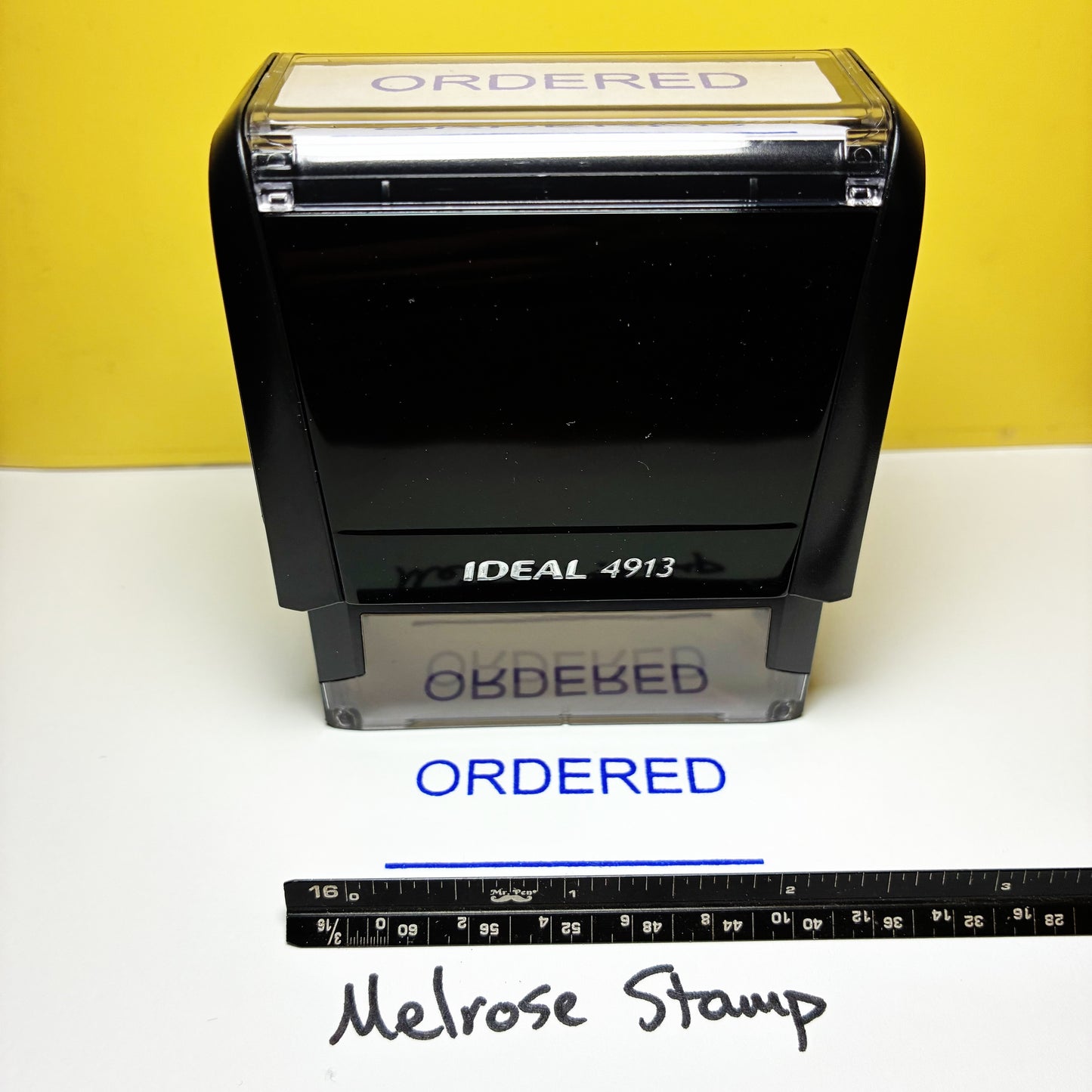 Black stamp labeled 'Ideal 4913' with 'ORDERED' text, next to a ruler for scale on a white background.