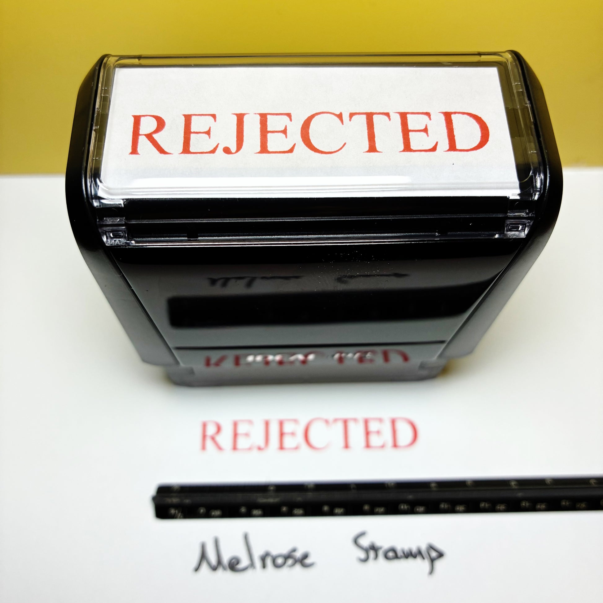 Stamp with 'REJECTED' text rubber stamp red ink and a ruler for size reference on a white paper 