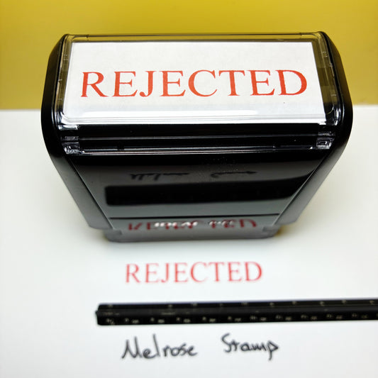 Stamp with 'REJECTED' text rubber stamp red ink and a ruler for size reference on a white paper 