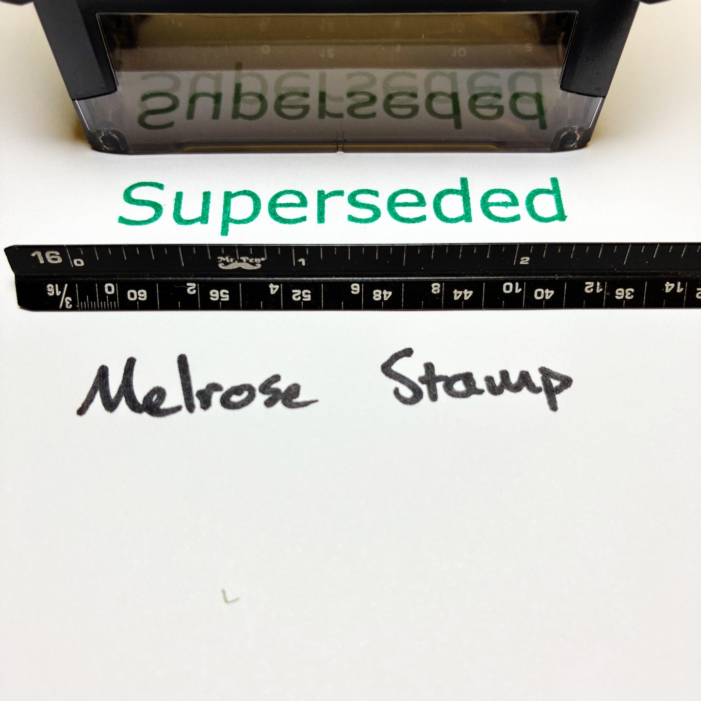 Melrose Stamp with 'Superseded' text rubber stamp green ink and a ruler for scale on a white background