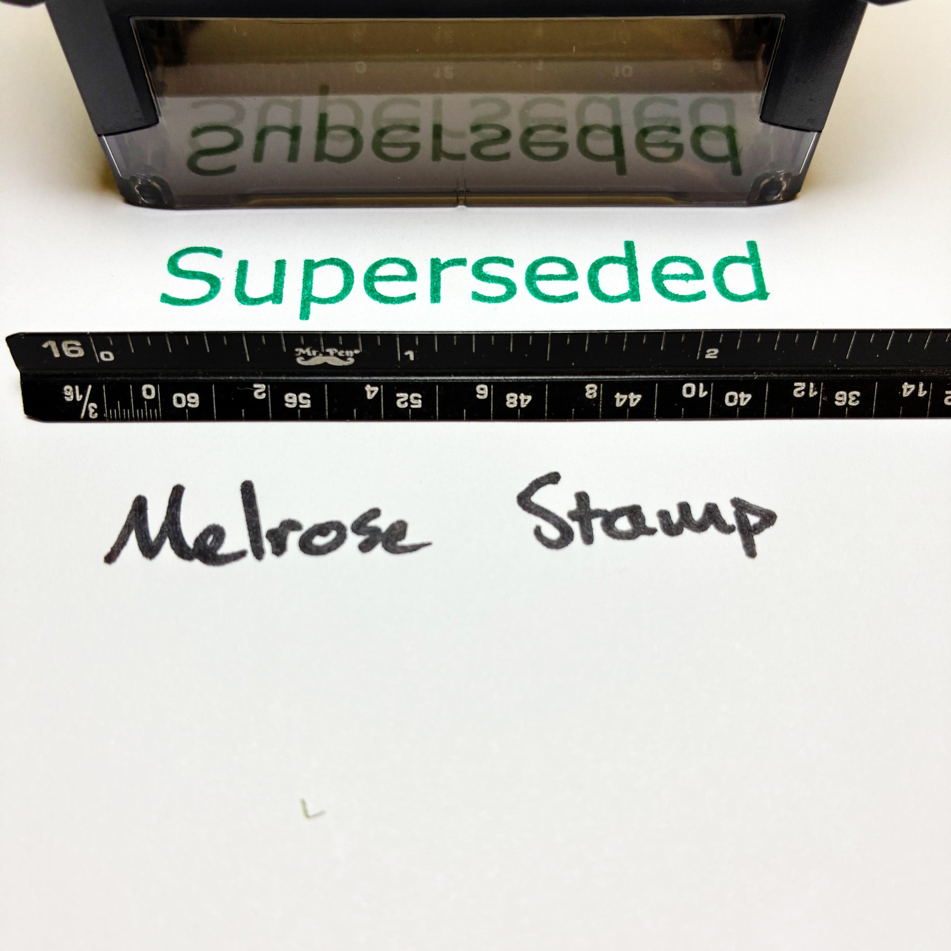 Melrose Stamp with 'Superseded' text rubber stamp green ink and a ruler for scale on a white background