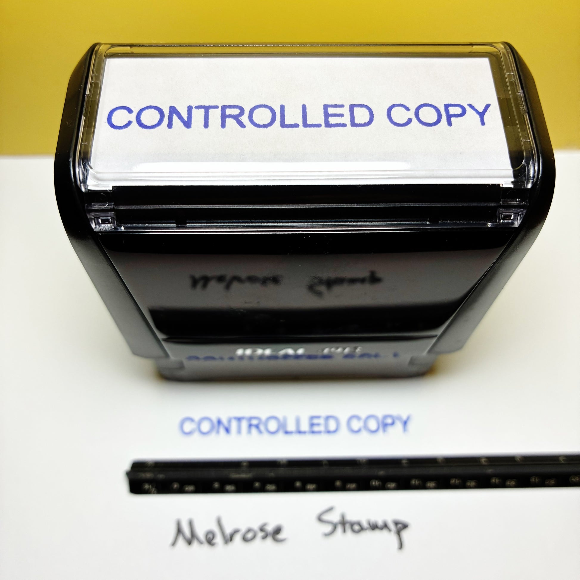 Stamp with 'CONTROLLED COPY' text blue ink and a ruler for scale on a white surface.