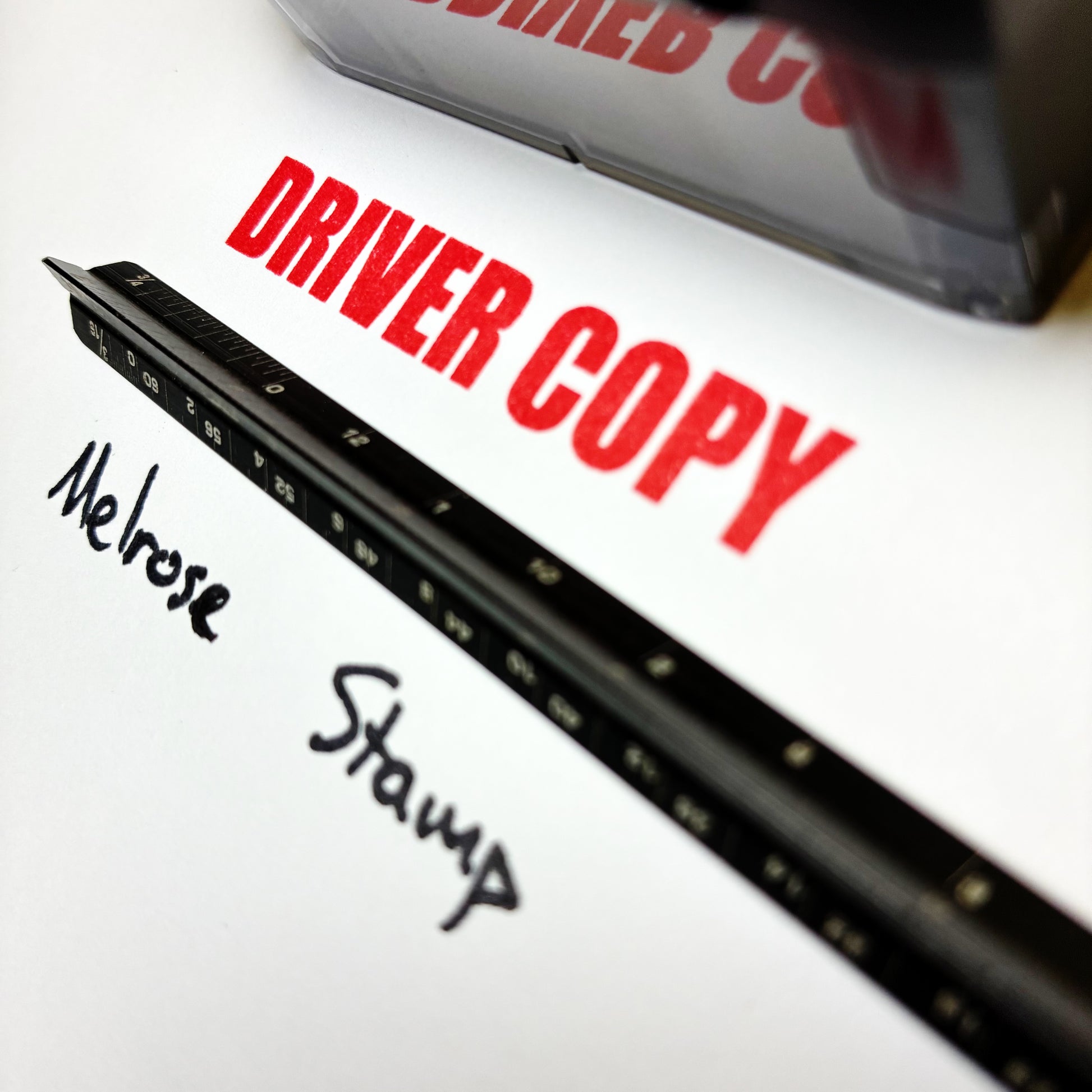 Close-up of a document with 'Driver Copy' and 'Melrose Stamp' text, featuring a black ruler rubber stamp red ink.