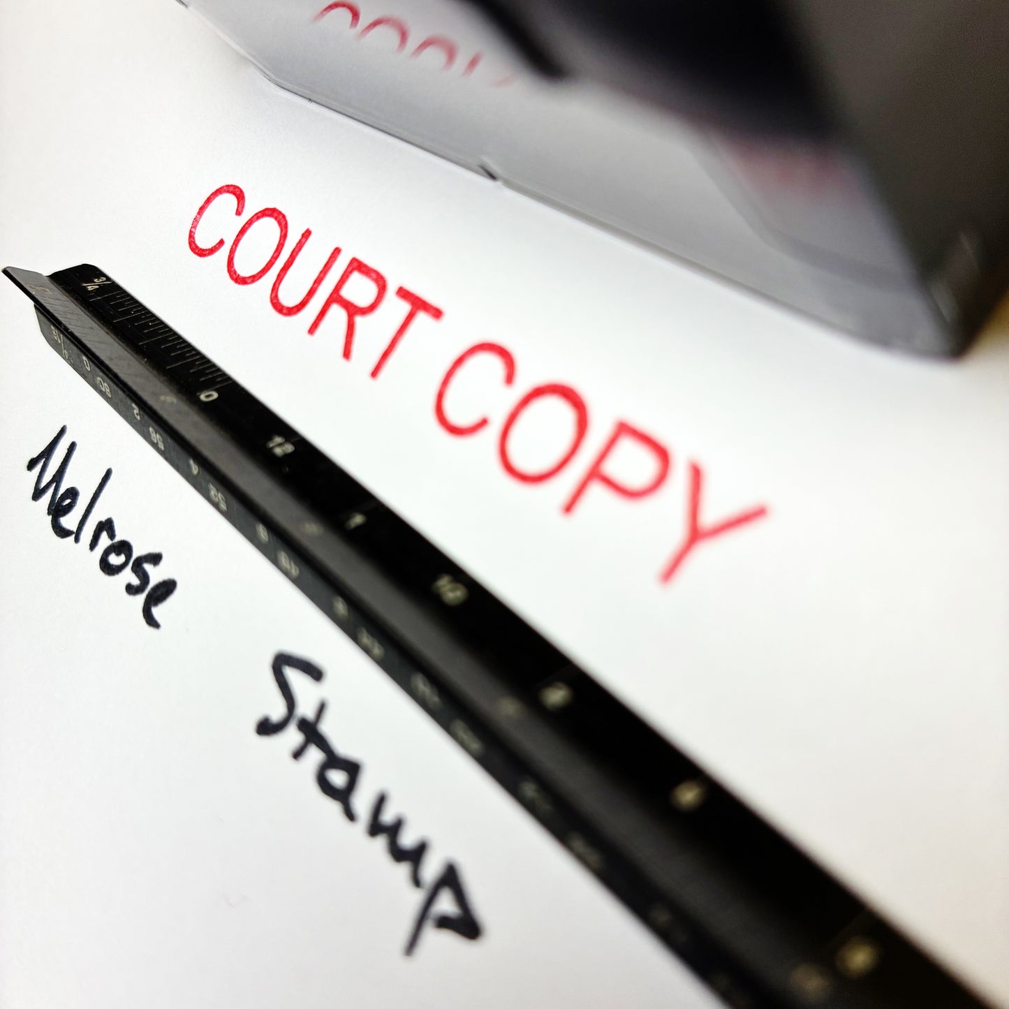 Close-up of a pen with text 'COURT COPY' and 'Melrose Stamp' on a white surface. rubber stamp red ink