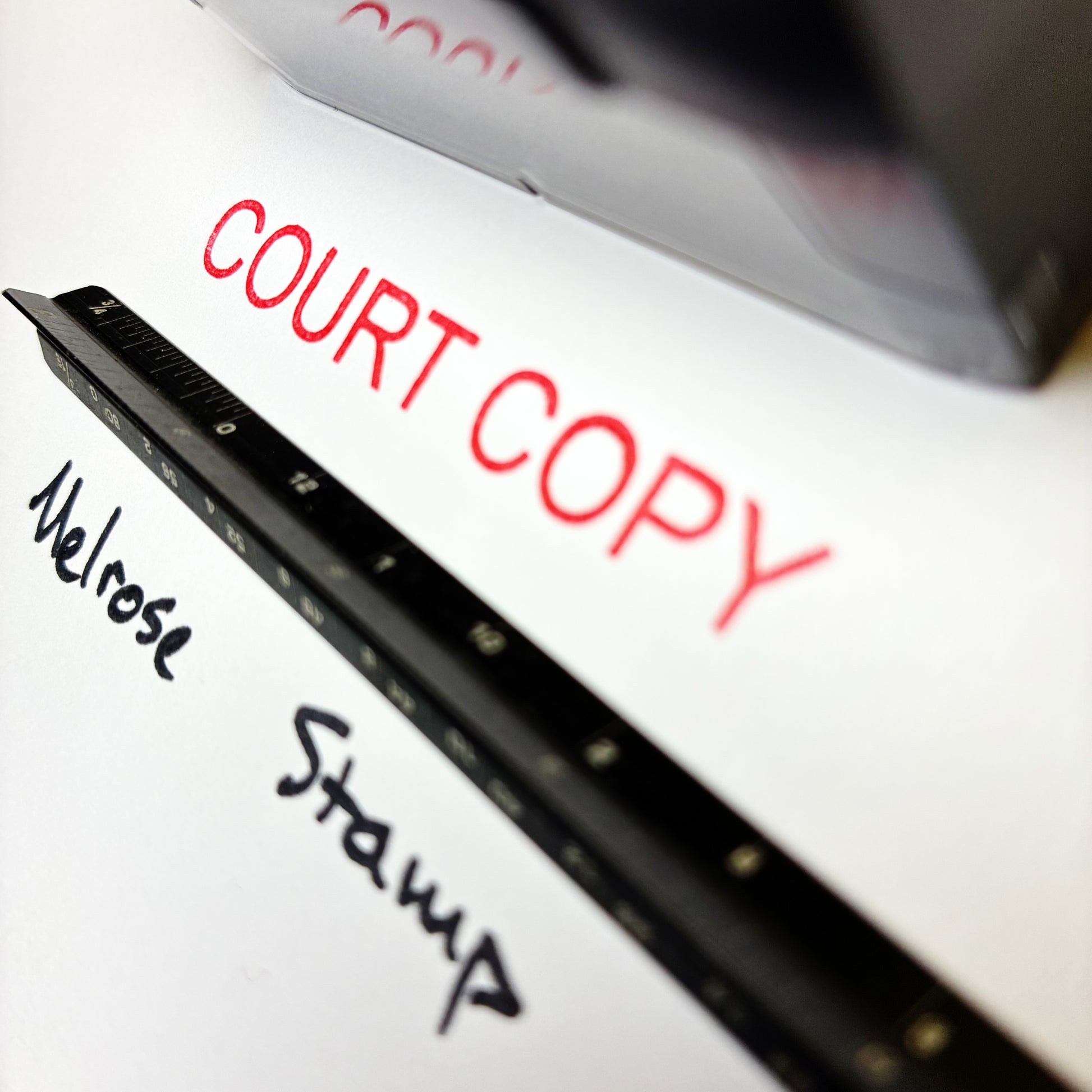 Close-up of a pen with text 'COURT COPY' and 'Melrose Stamp' on a white surface. rubber stamp red ink