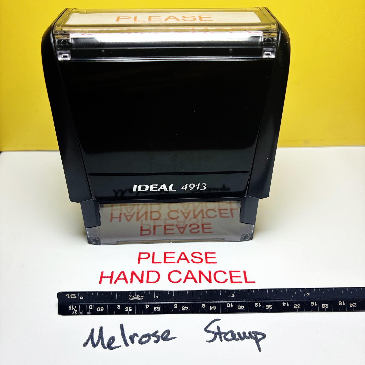 Black stamp with 'PLEASE HAND CANCEL' text on a white surface with a yellow rubber stamp red ink background