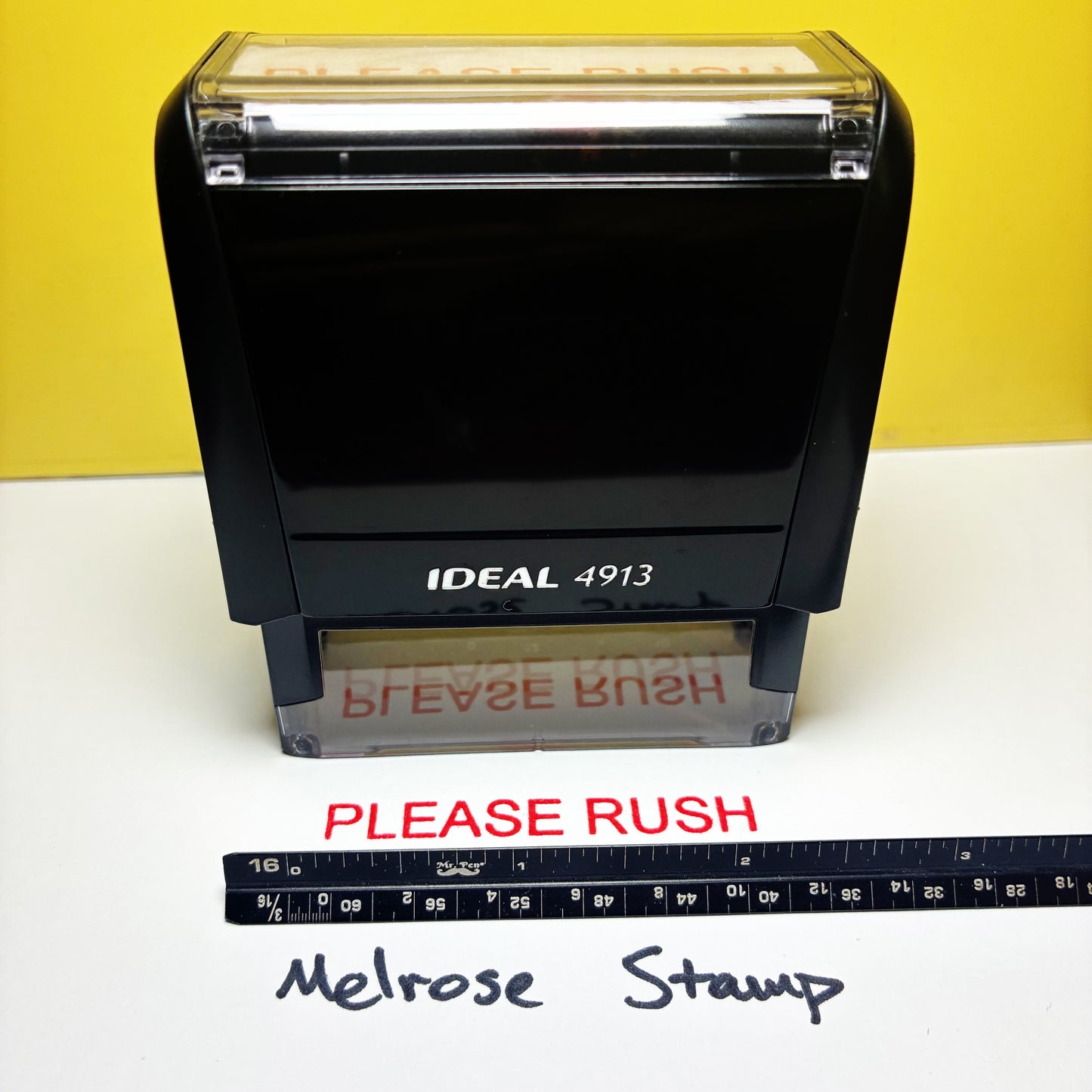 Black stamp with 'PLEASE RUSH' text and ruler for scale on a yellow background red ink
