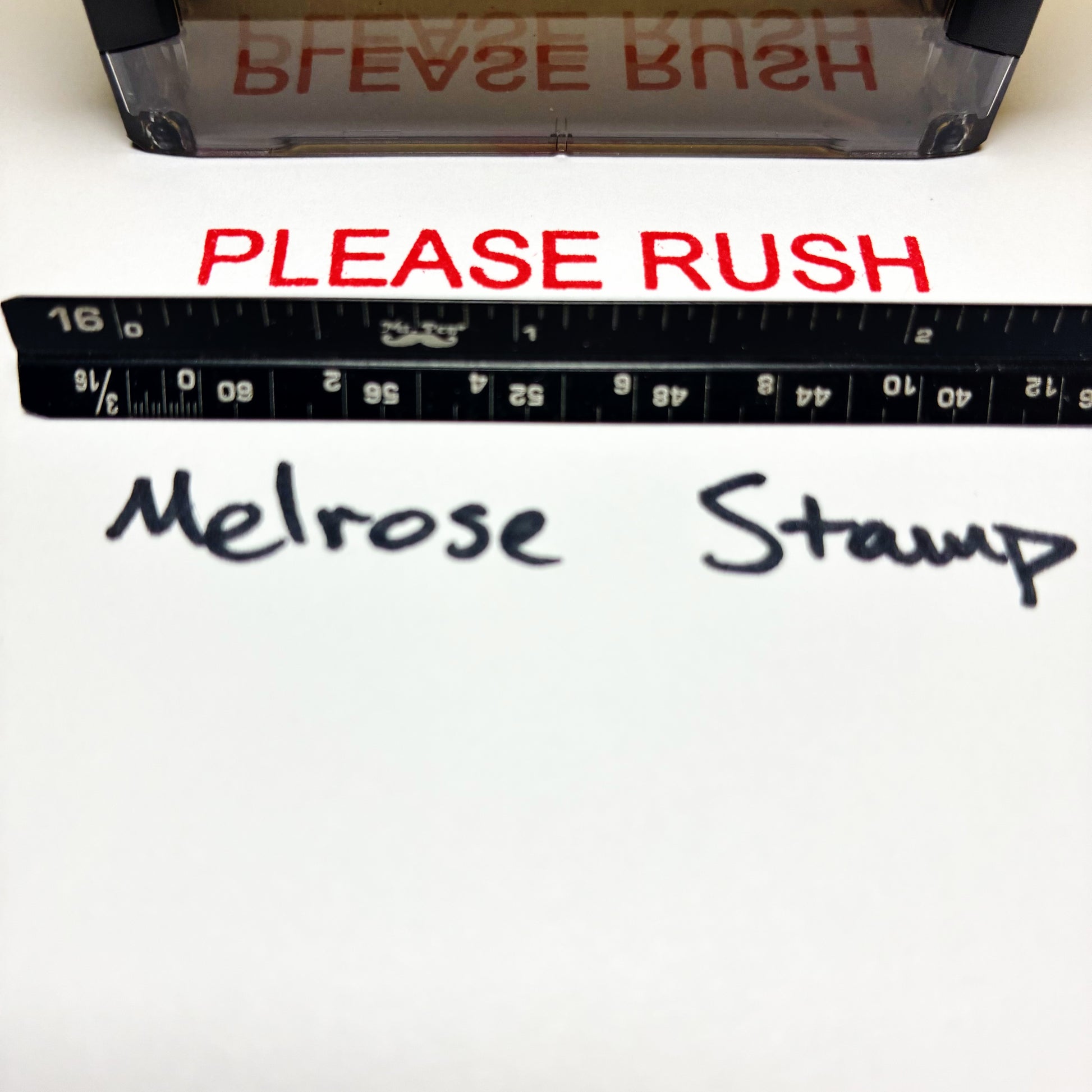 Stamp with 'PLEASE RUSH' text and a ruler below, on a white background.