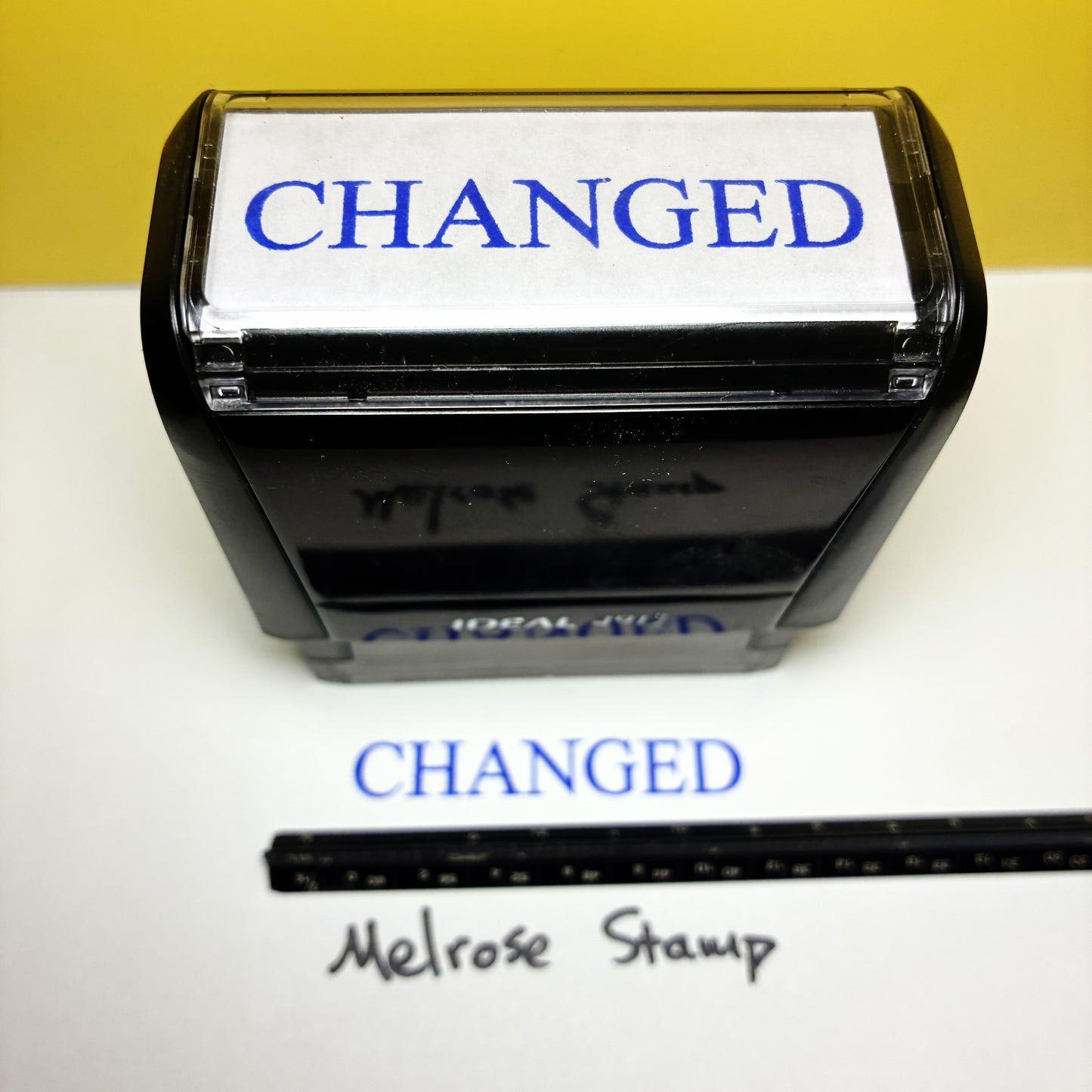 Rubber stamp with 'CHANGED' text blue ink and a ruler below on a white background