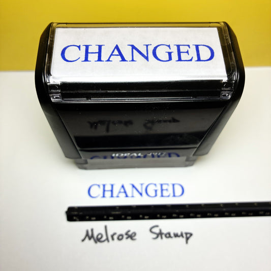 Rubber stamp with 'CHANGED' text blue ink and a ruler below on a white background