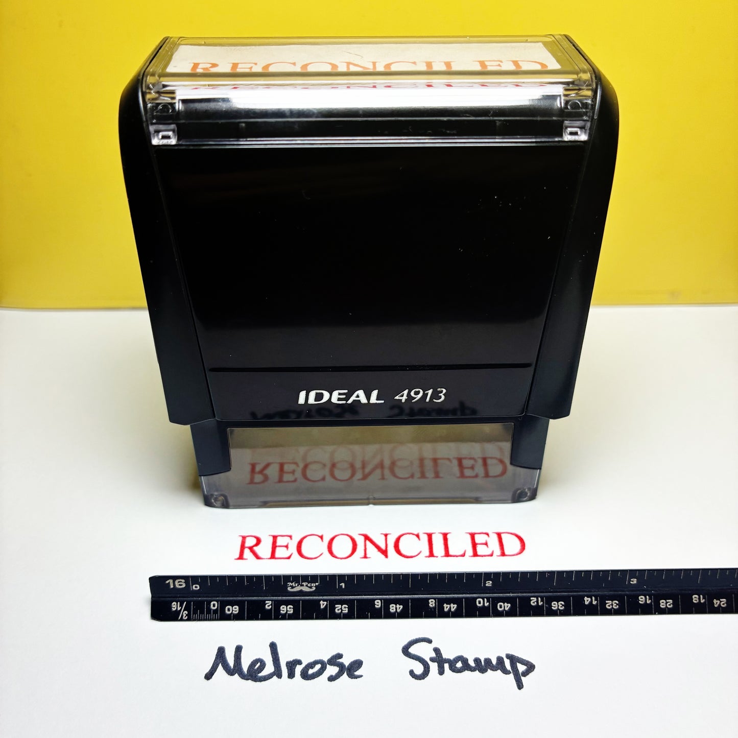 Rubber stamp with 'RECONCILED' text on a yellow and white background, featuring an ruler for scale.