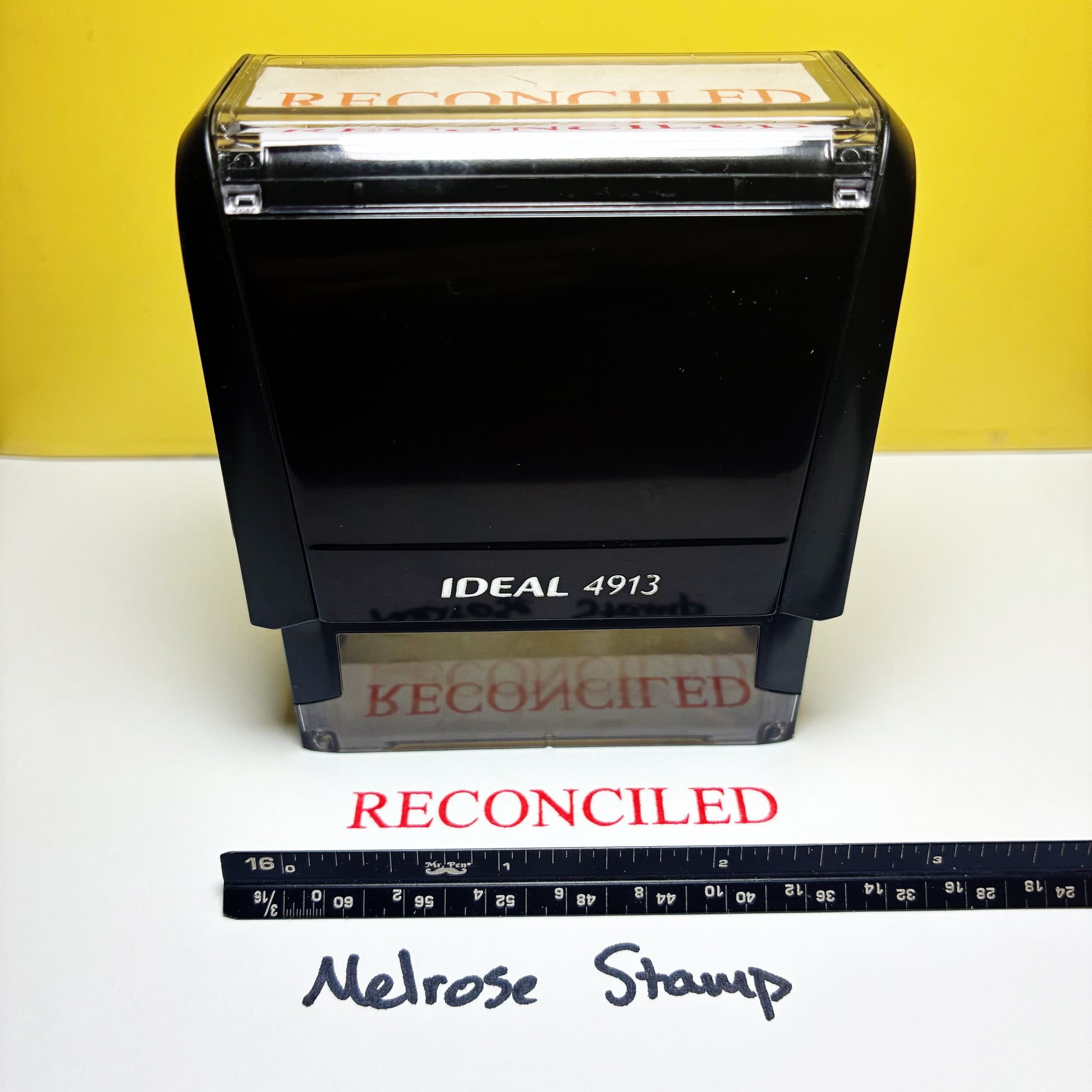 Rubber stamp with 'RECONCILED' text on a yellow and white background, featuring an ruler for scale.