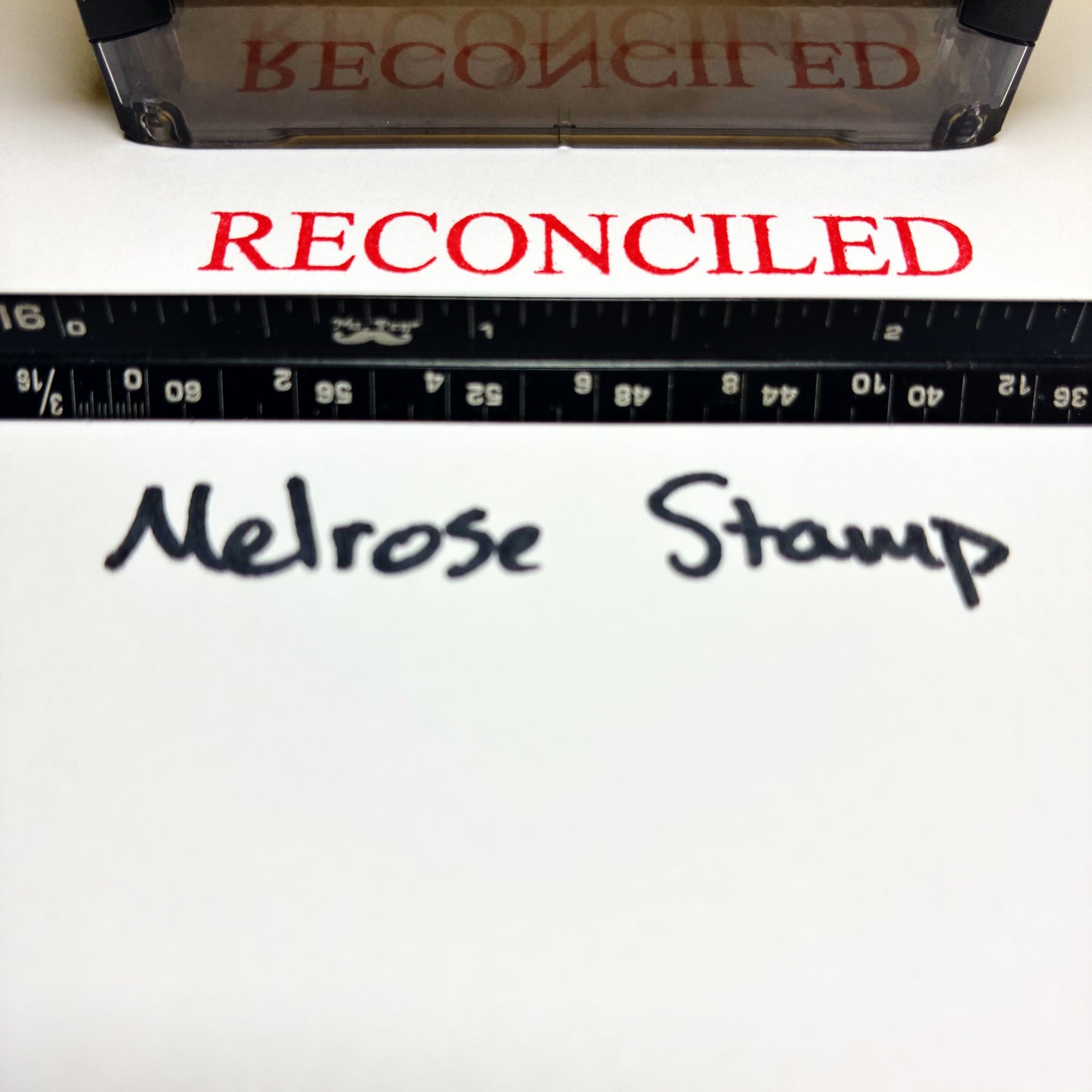 Rubber stamp with 'RECONCILED' text and a ruler below on a white background.