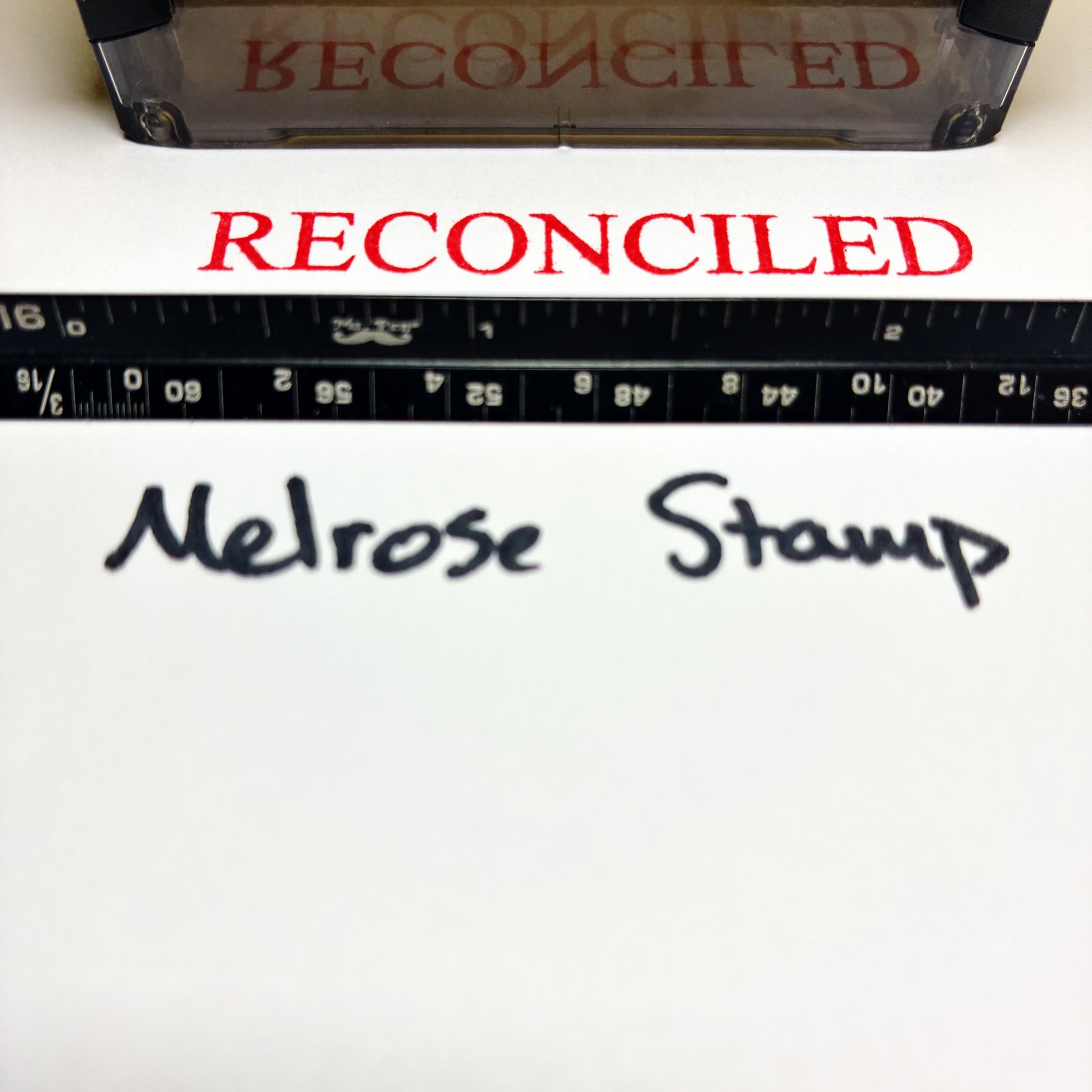 Rubber stamp with 'RECONCILED' text and a ruler below on a white background.