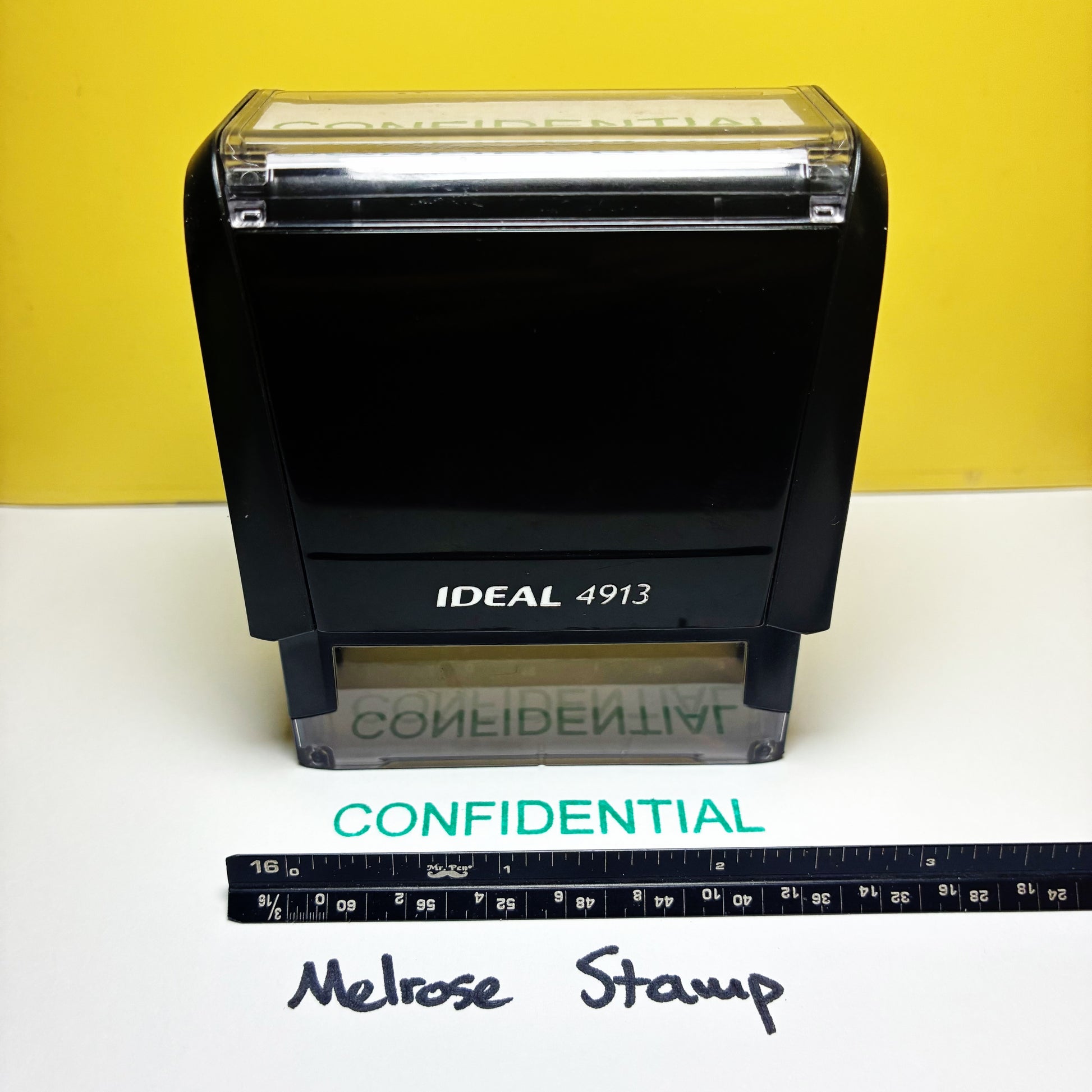 Rubber stamps Ideal 4913  with 'CONFIDENTIAL' text green ink on a white surface with a yellow background.
