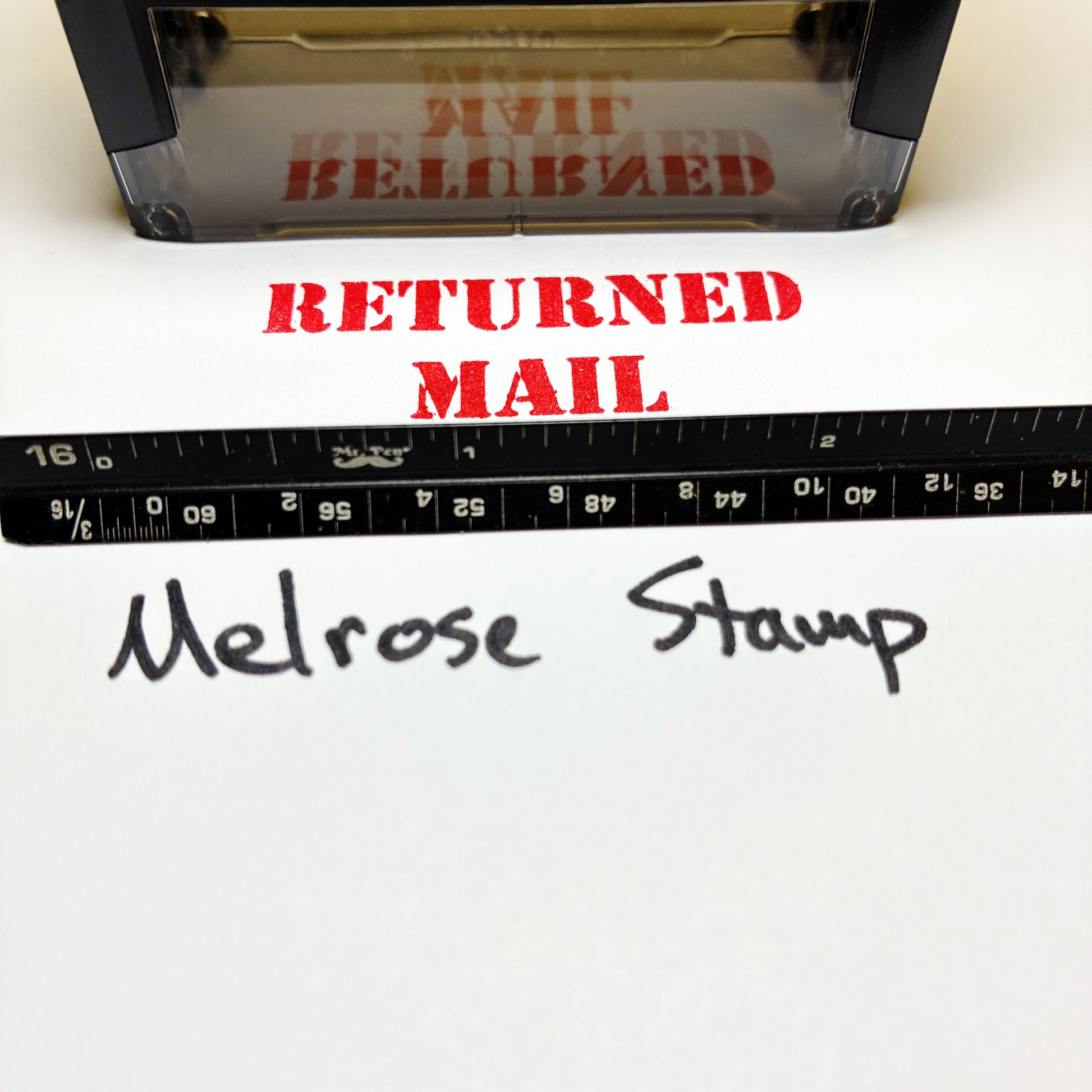 Rubber Stamp with 'RETURNED MAIL' text and a ruler below, on a white background.