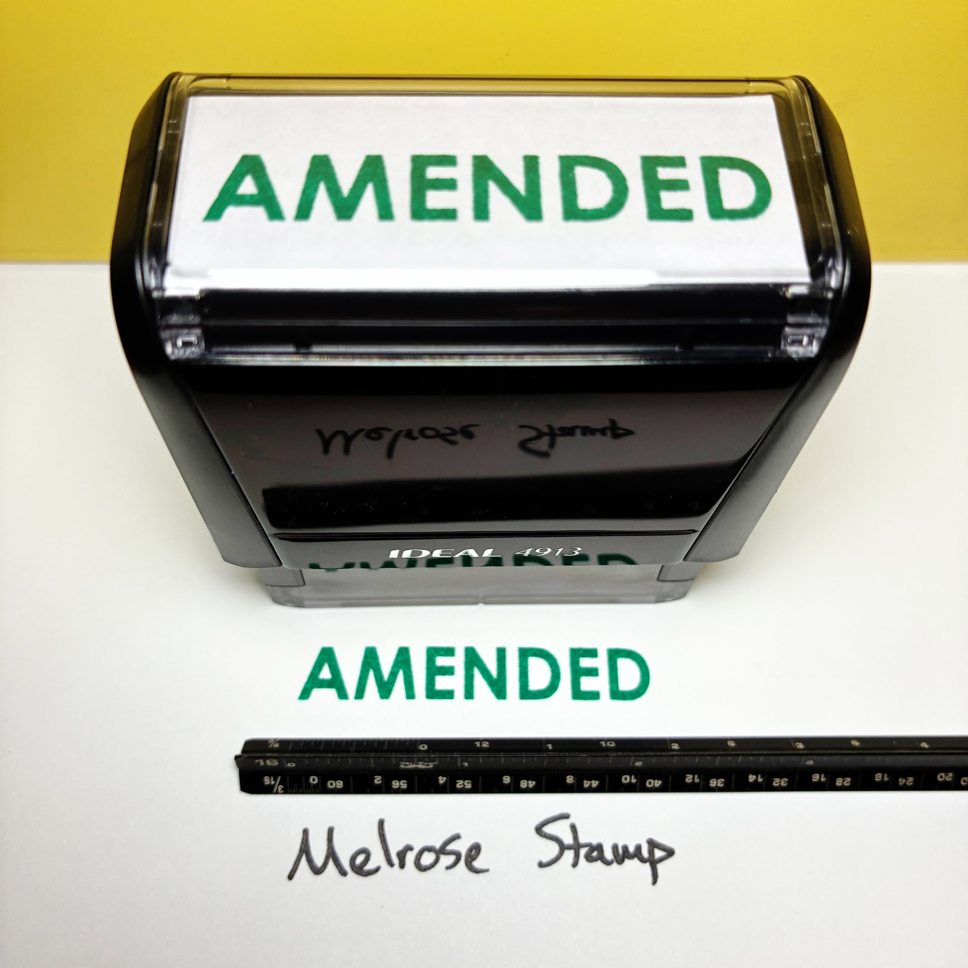 Self-inking rubber stamp with 'AMENDED' green ink on a white background
