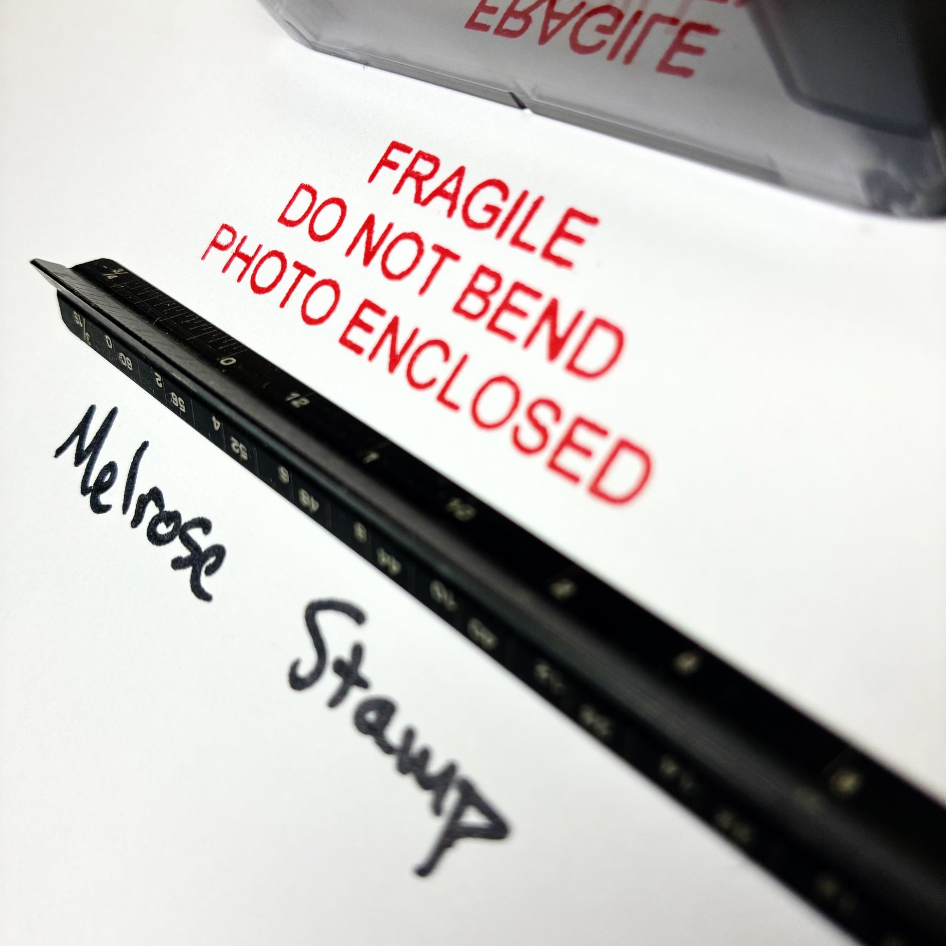 Close-up of a package with 'Fragile Do Not Bend Photo Enclosed' text and 'Melrose Stump' branding.