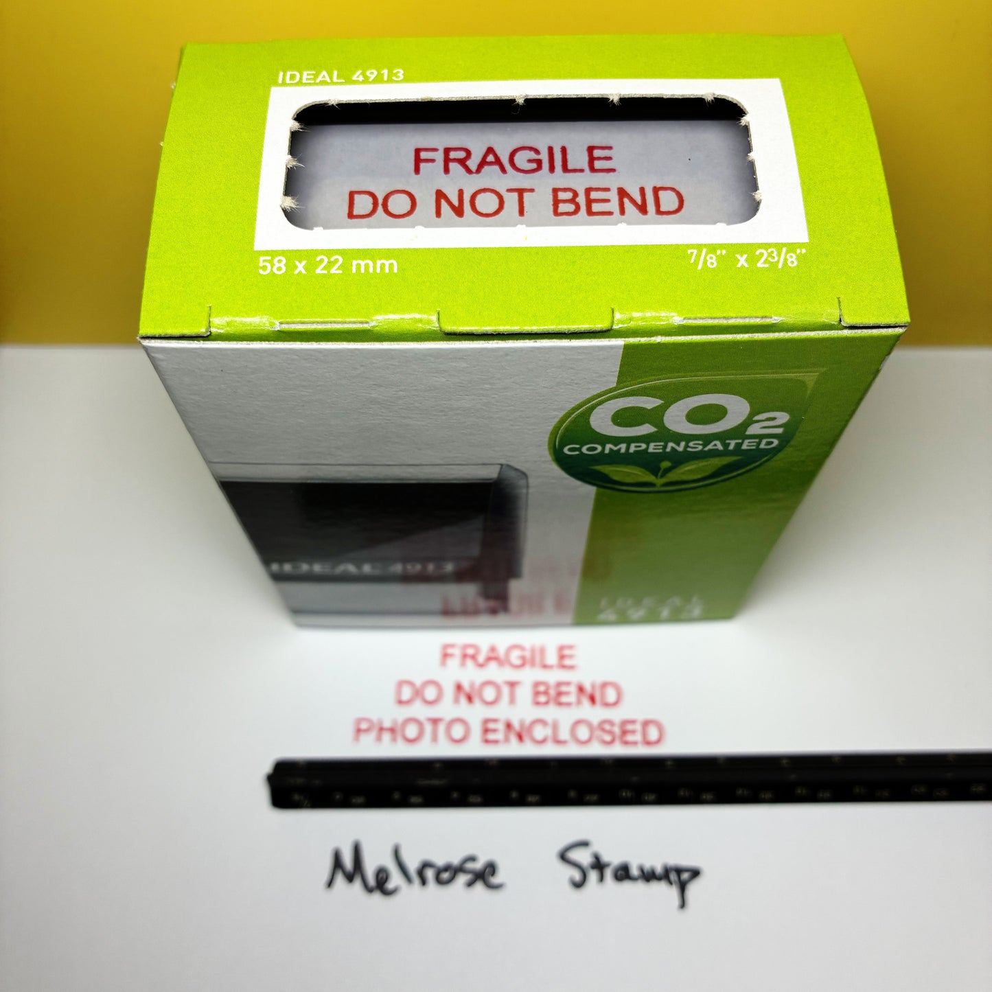 Green box with 'Fragile Do Not Bend Photo Enclosed' rubber stamp red ink self-inking on a white surface