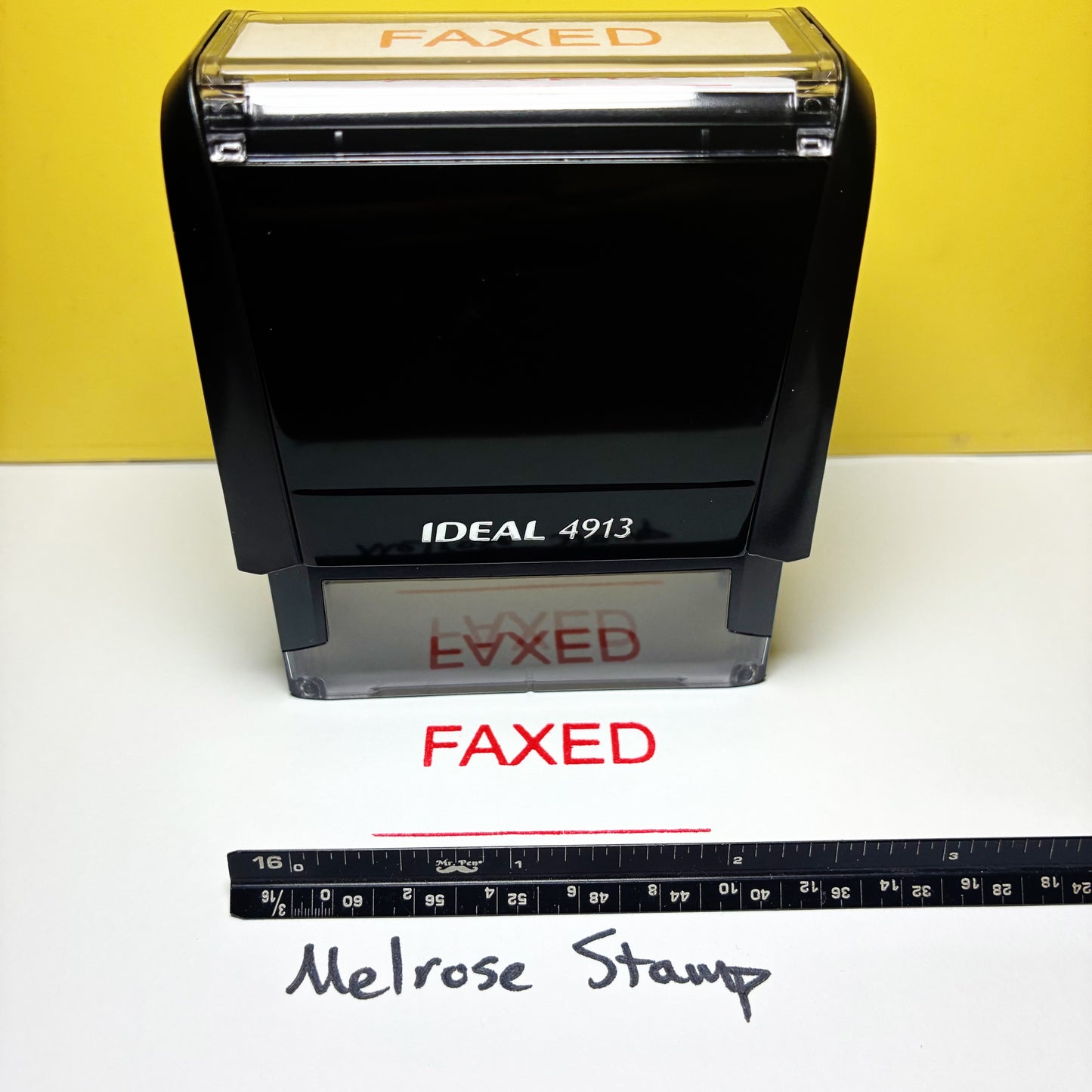 Rubber stamp labeled 'FAXED' with a ruler for scale on a white surface.