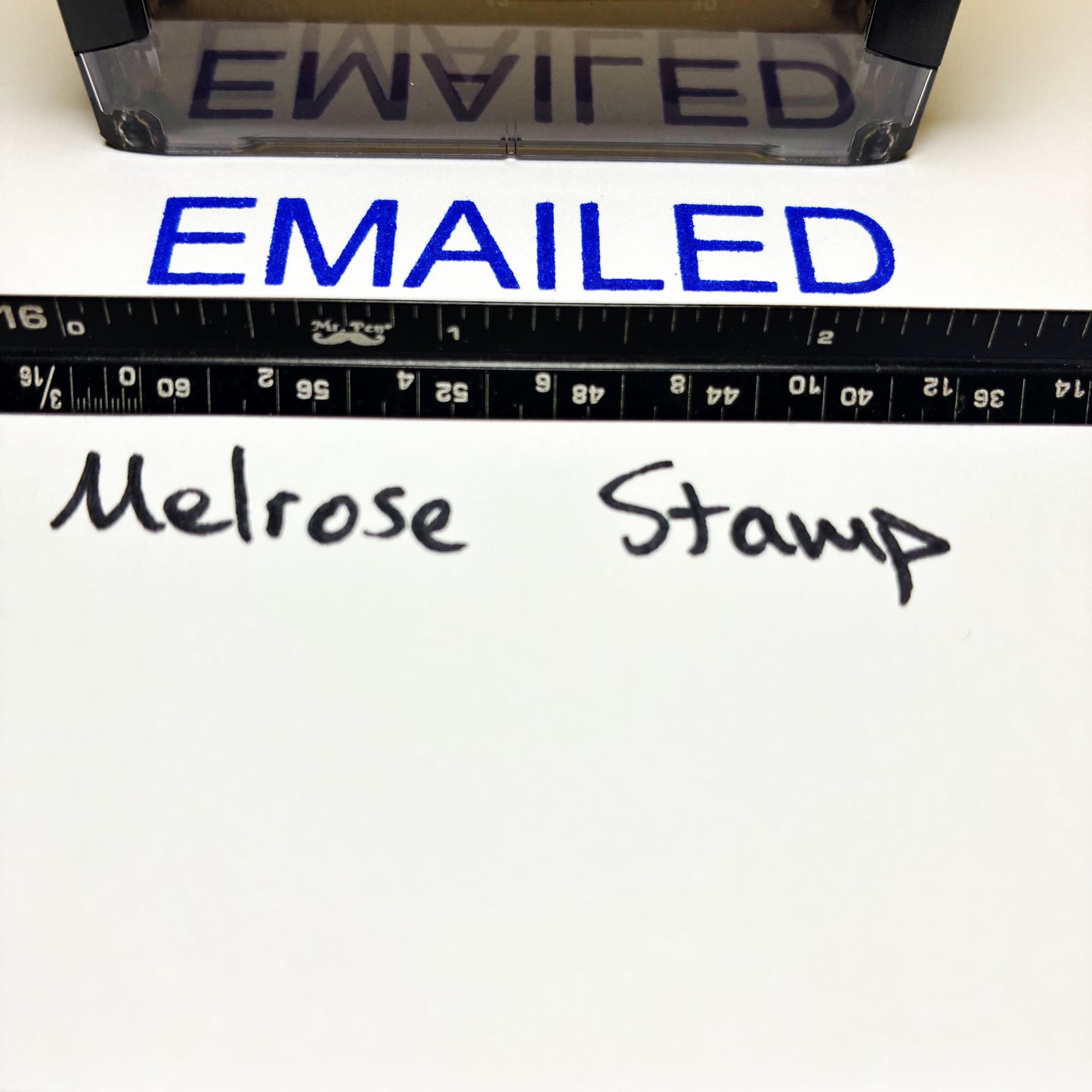 Rubber stamp with 'EMAILED' text blue ink and a ruler below on a white background.