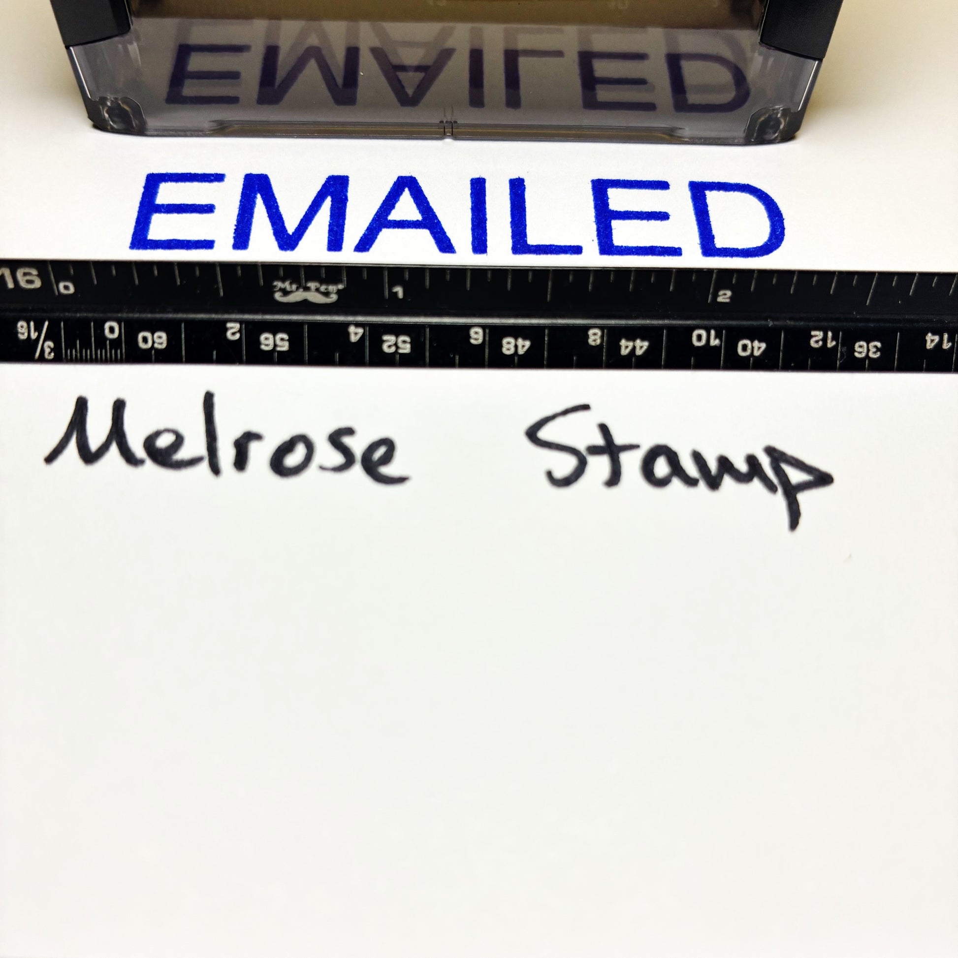Rubber stamp with 'EMAILED' text blue ink and a ruler below on a white background.