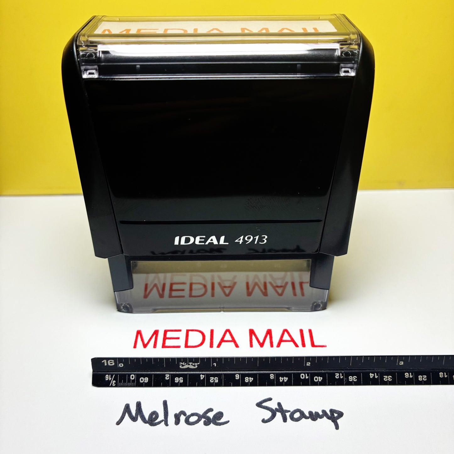 Rubber stamp with 'MEDIA MAIL' text red ink on a yellow background