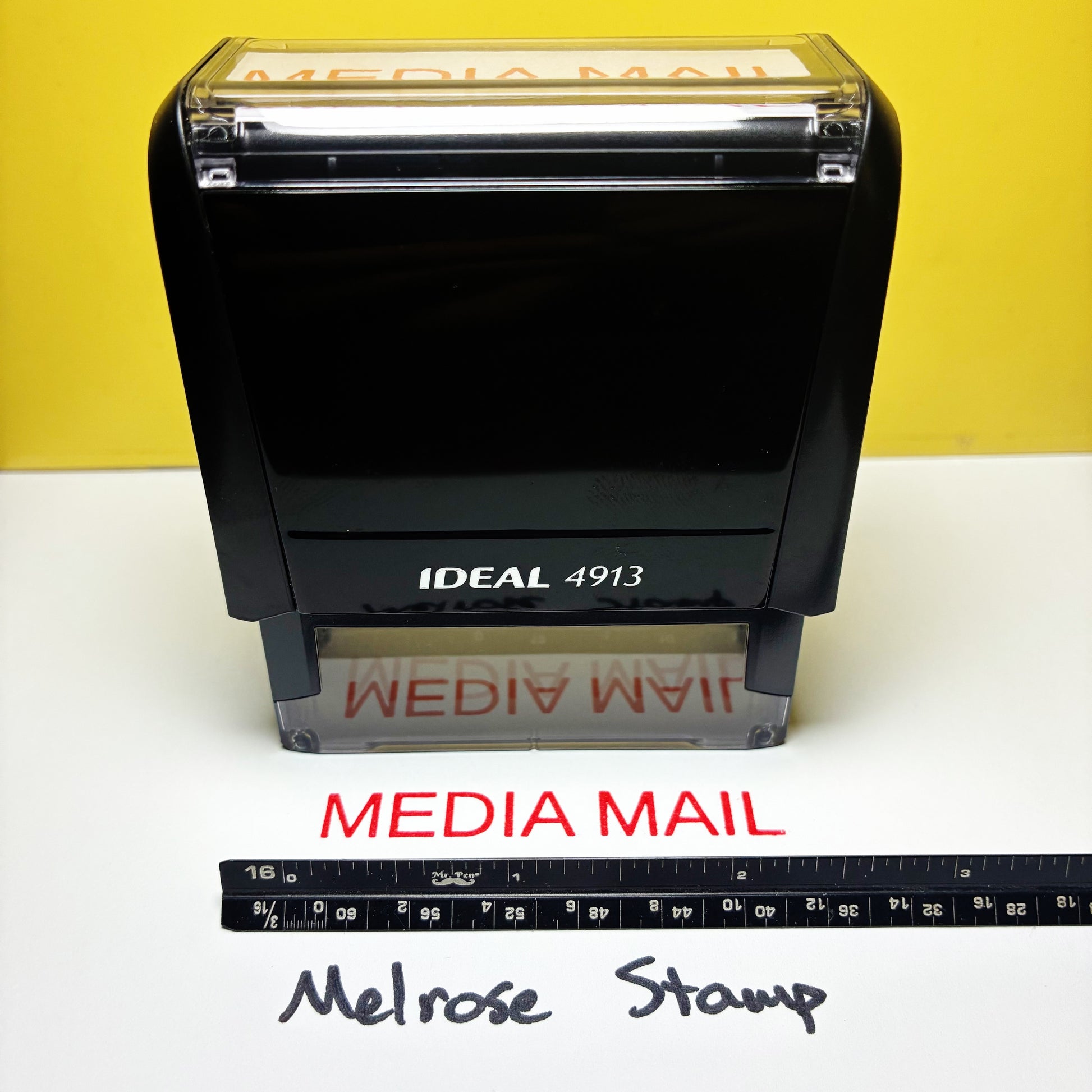 Rubber stamp with 'MEDIA MAIL' text red ink on a yellow background