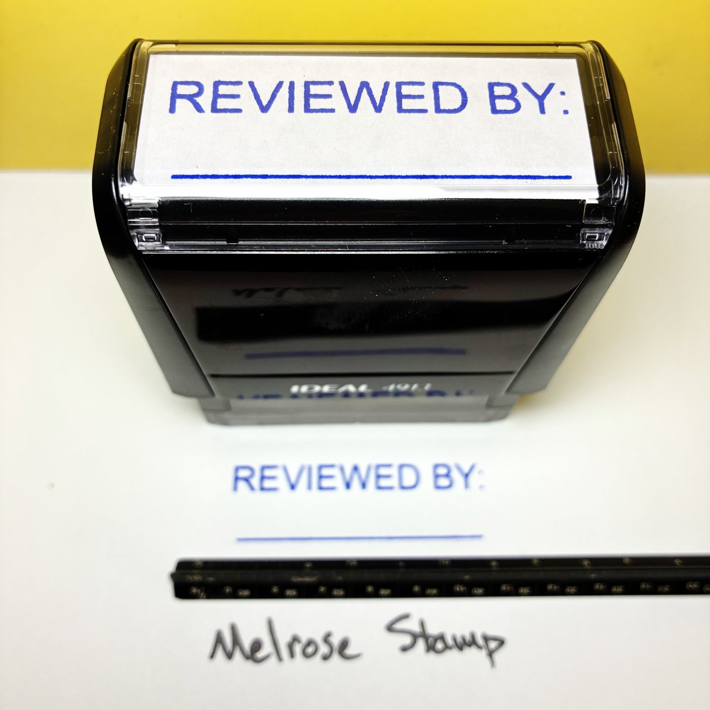 Rubber stamp with 'REVIEWED BY:' text on a white background, next to a ruler for scale.