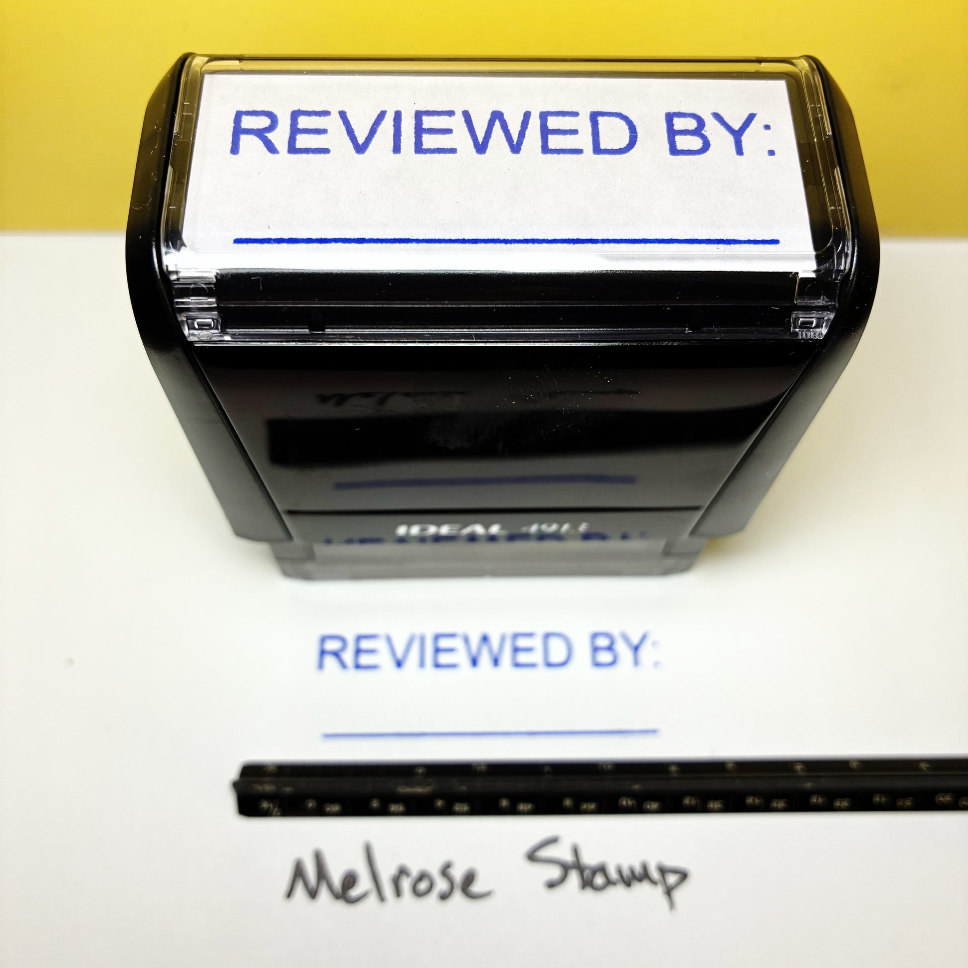 Rubber stamp with 'REVIEWED BY:' text on a white background, next to a ruler for scale.