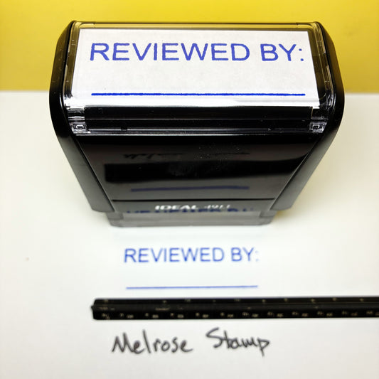 Rubber stamp with 'REVIEWED BY:' text on a white background, next to a ruler for scale.