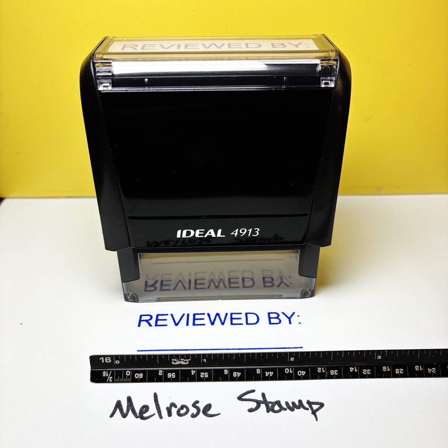 Rubber stamp with 'REVIEWED BY' text on a white surface with a yellow background