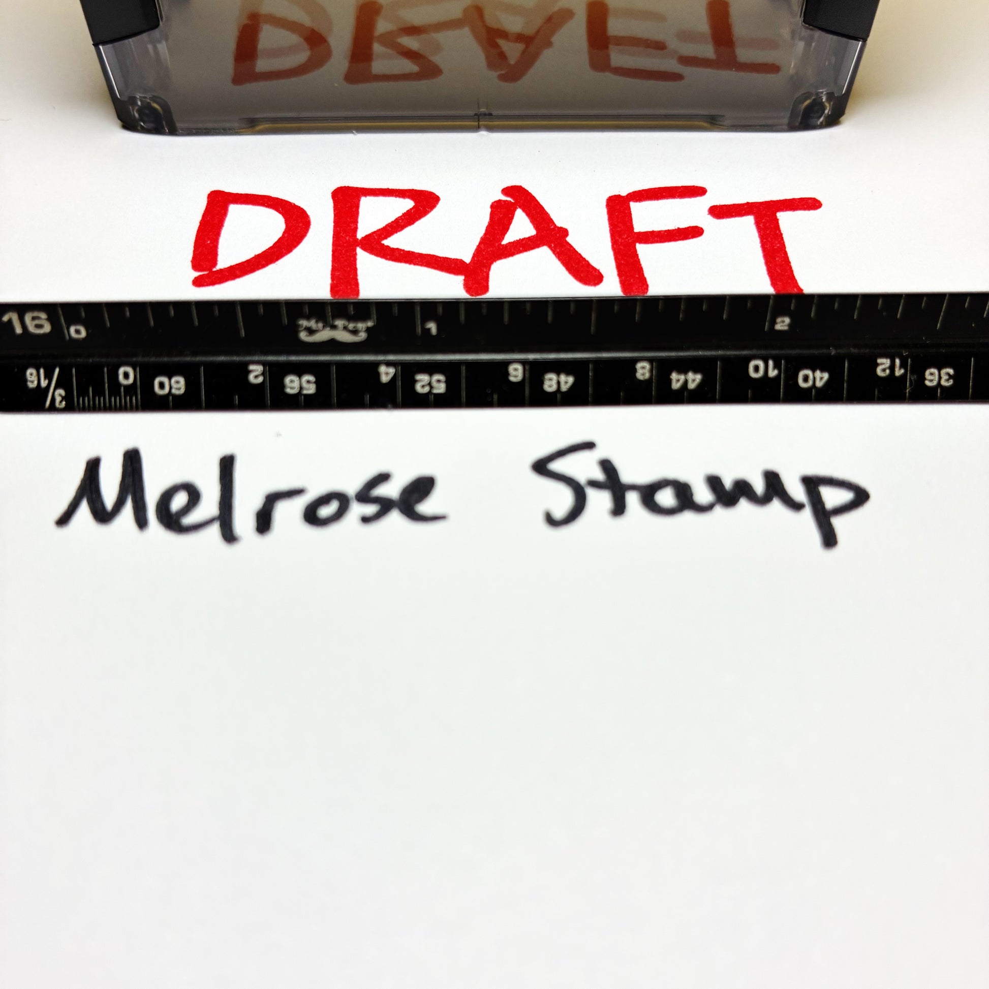 Red 'DRAFT' text on paper with a ruler and 'Melrose Stamp' branding.