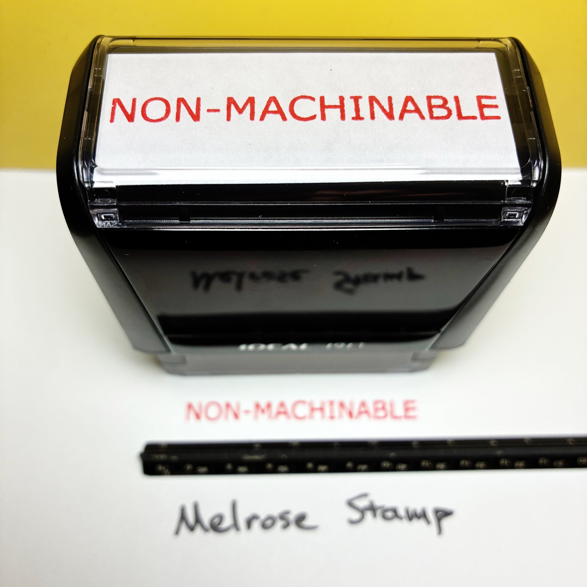 Rubber stamp with 'NON-MACHINABLE' text on a white surface, with a yellow background.