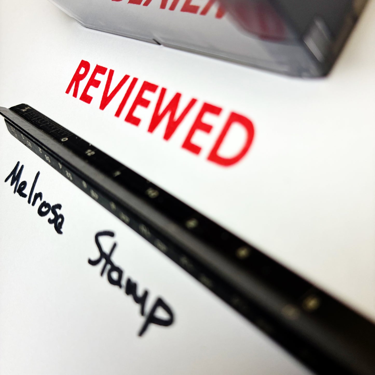 Close-up of a stamp with 'REVIEWED' in red and 'Melrose Stamp' in black, on a white background.