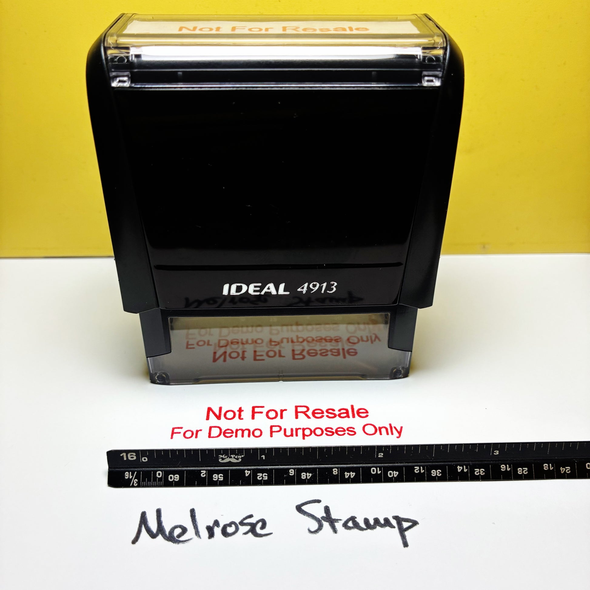 A black self-inking stamp labeled IDEAL 4913, shown on a white surface with a yellow background. Red text below reads 'Not For Resale For Demo Purposes Only,' and a measuring ruler and handwritten 'Melrose Stamp' are visible in front.