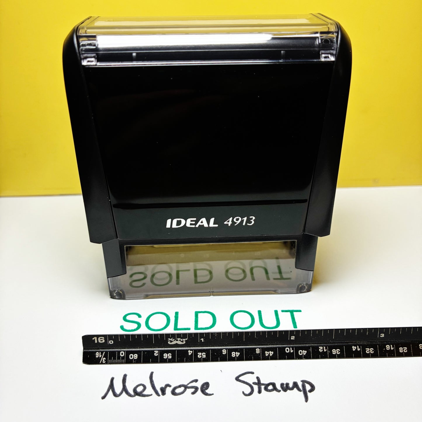 Black stamp with 'SOLD OUT' text on a white surface against a yellow background