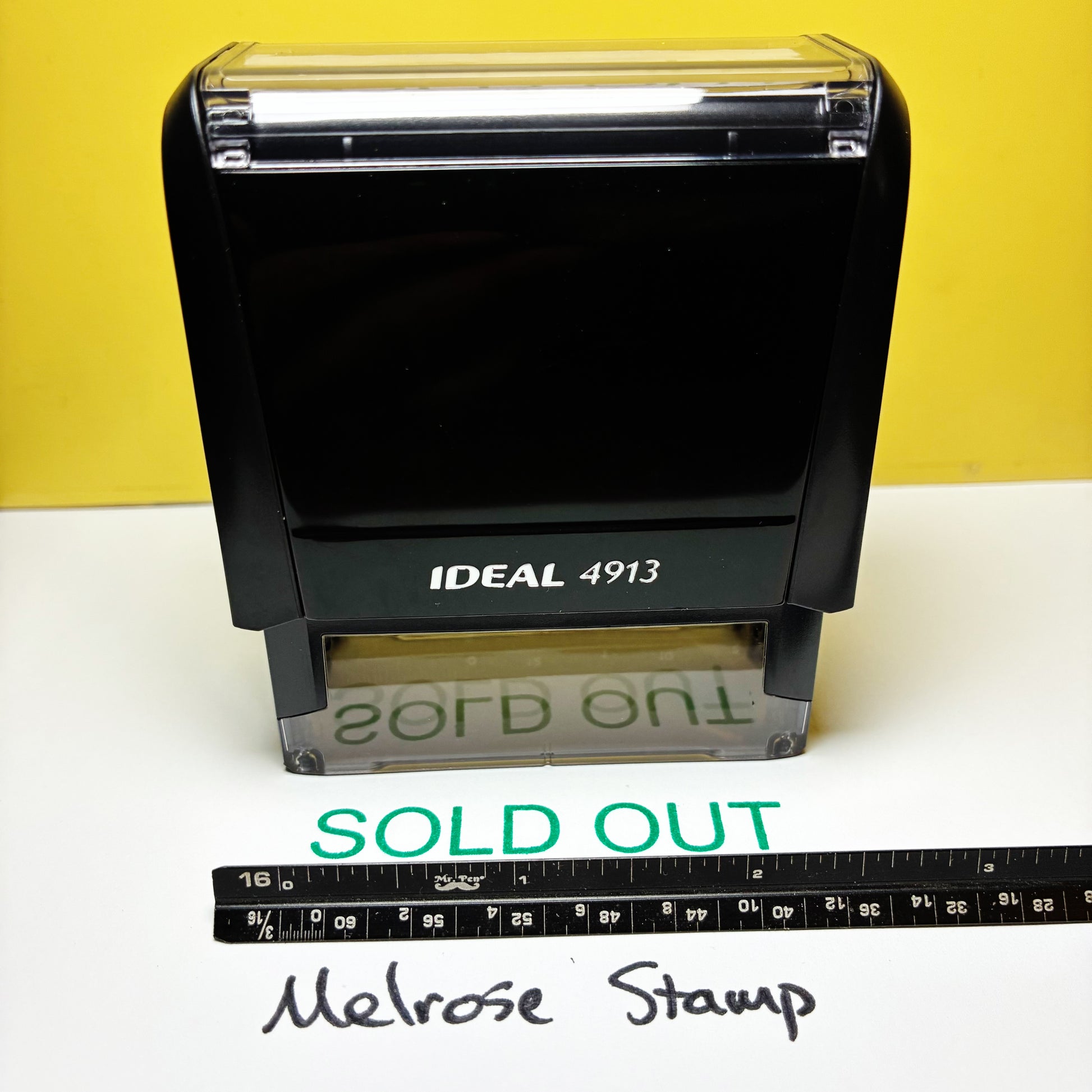Black stamp with 'SOLD OUT' text on a white surface against a yellow background