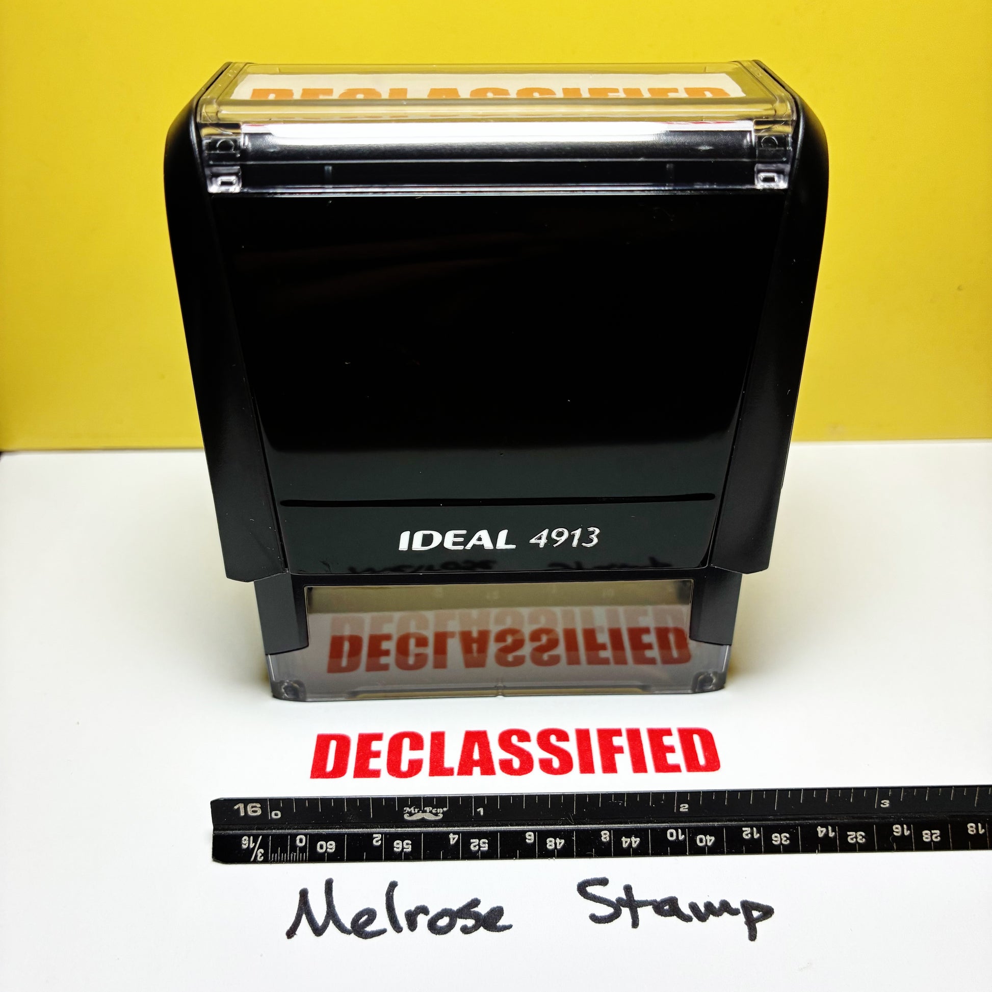 Rubber stamp labeled 'DECLASSIFIED' with a ruler for scale on a white background