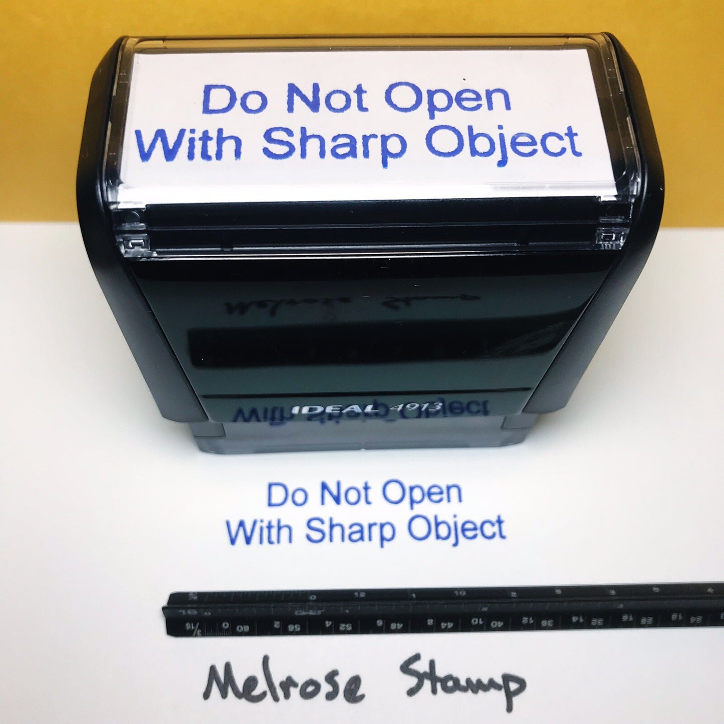 Self-inking stamp with 'Do Not Open With Sharp Object' text and a ruler for scale.