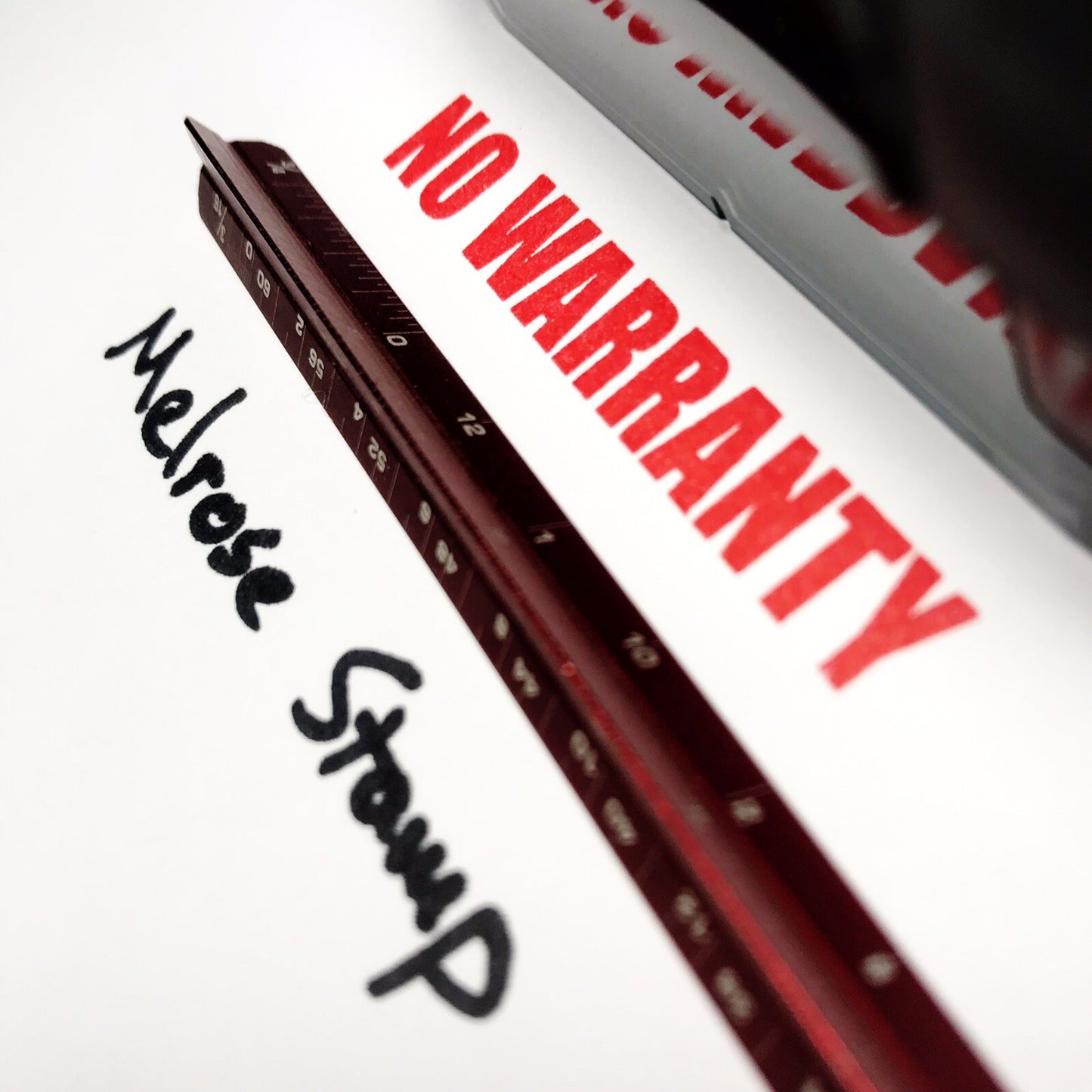Close-up of a red ruler with 'No Warranty' text and 'Melrose Stamp' branding.