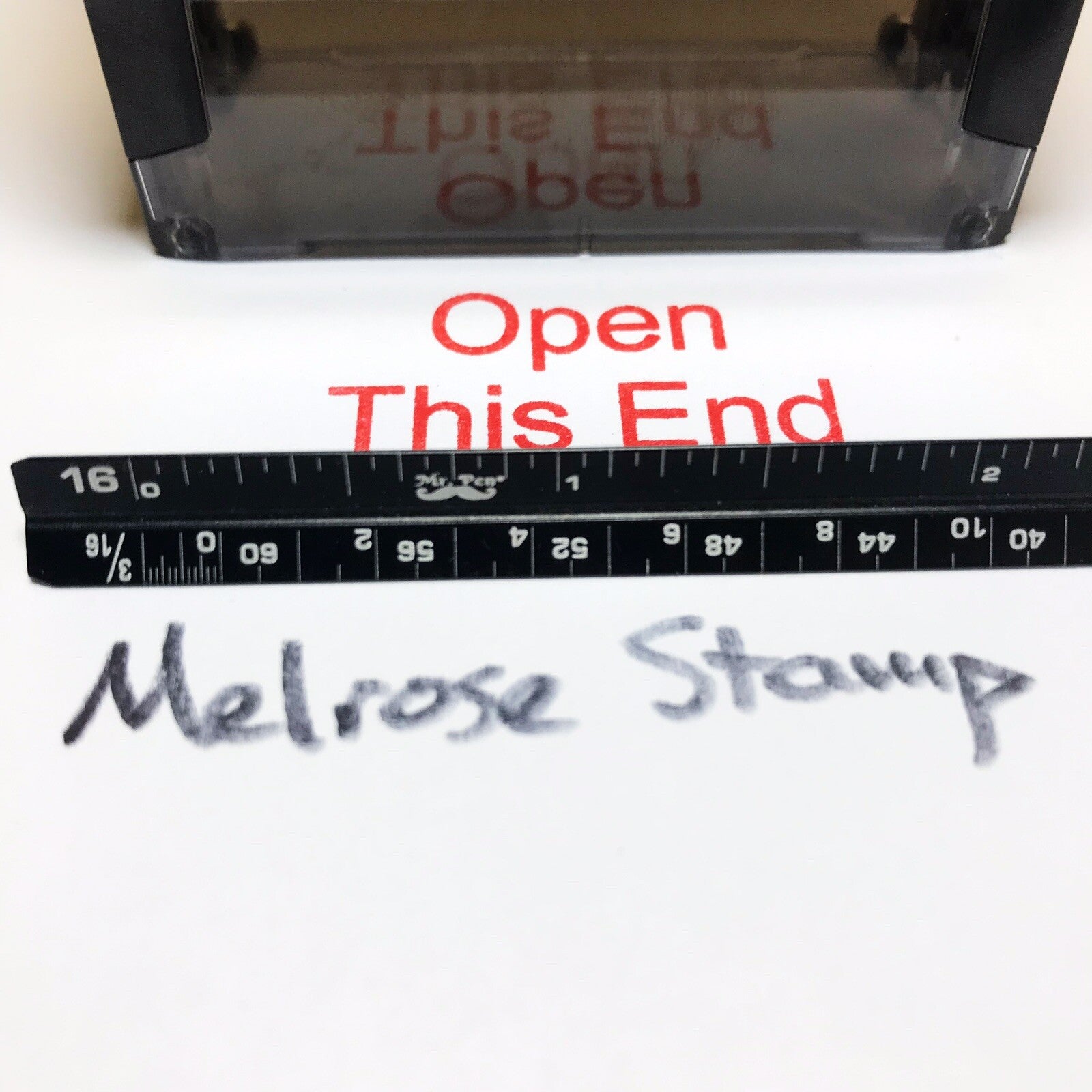 Open This End stamp impression with Melrose Stamp on paper close up with ruler