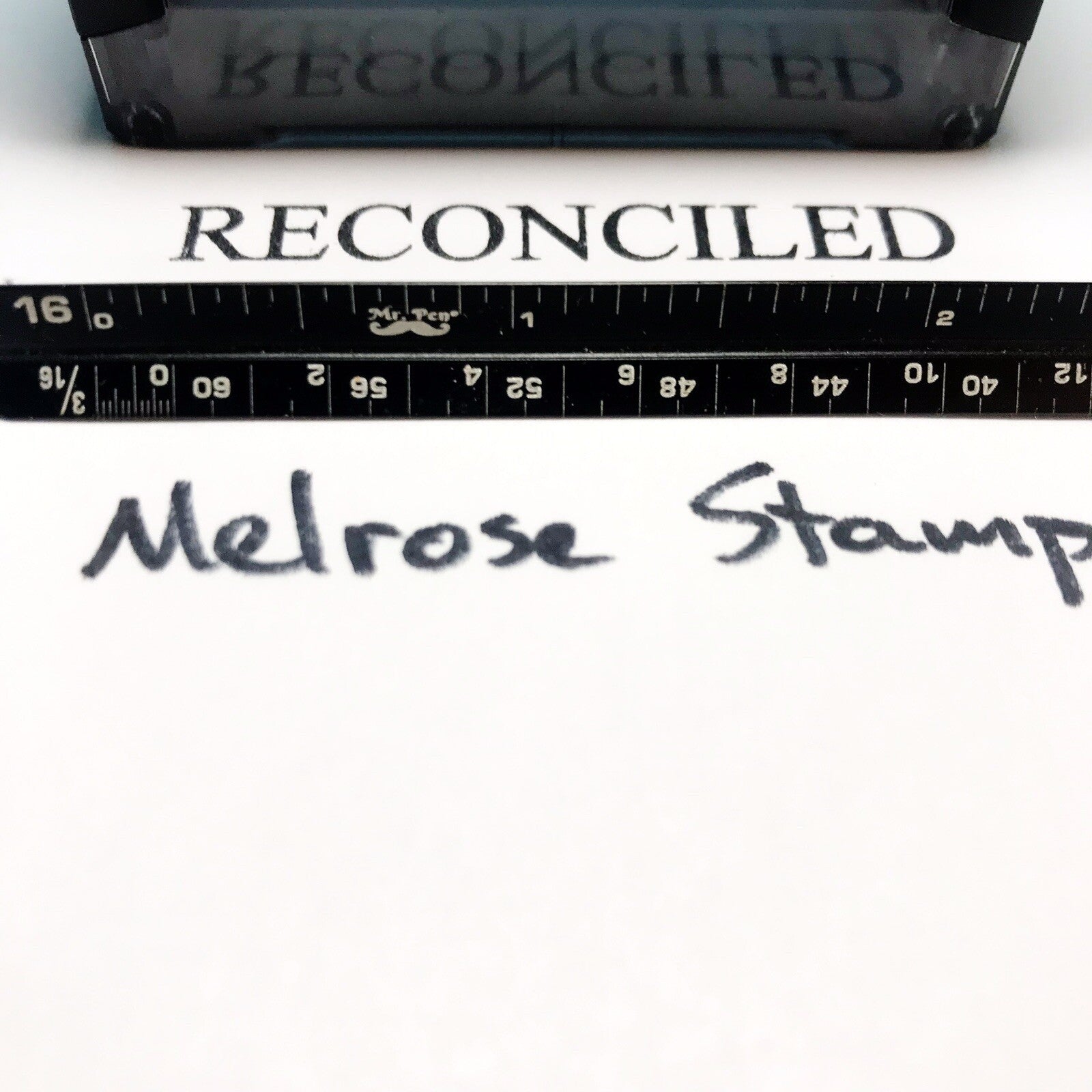 Rubber stamp with 'RECONCILED' text and a ruler below on a white background