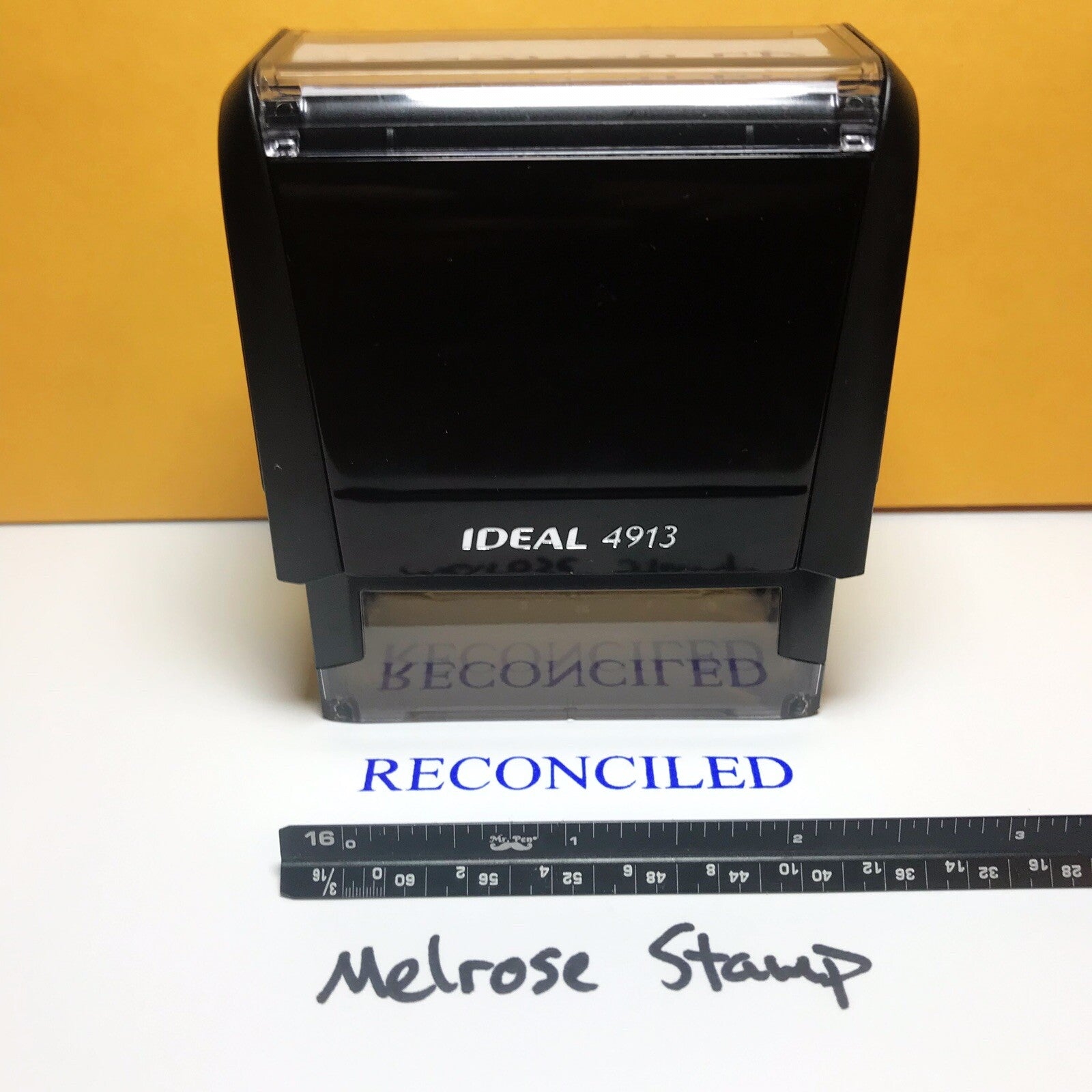 Black stamp with 'RECONCILED' text and a ruler for size reference on a white surface.