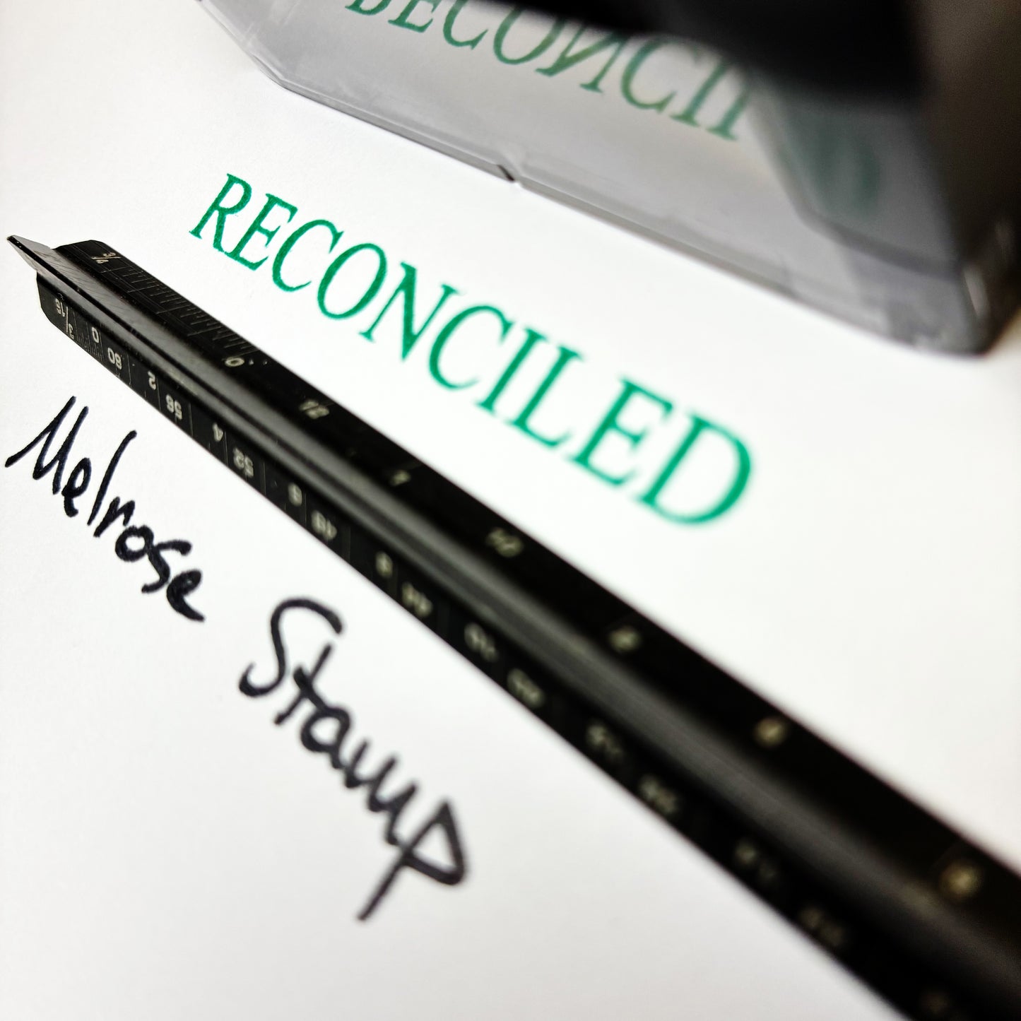 Close-up of a stamp with 'RECONCILED' and 'Melrose Stamp' text on a white background.