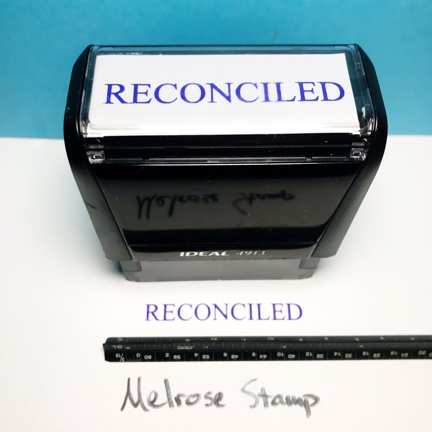 Rubber stamp with 'RECONCILED' text and a ruler for size reference on a blue and white background.